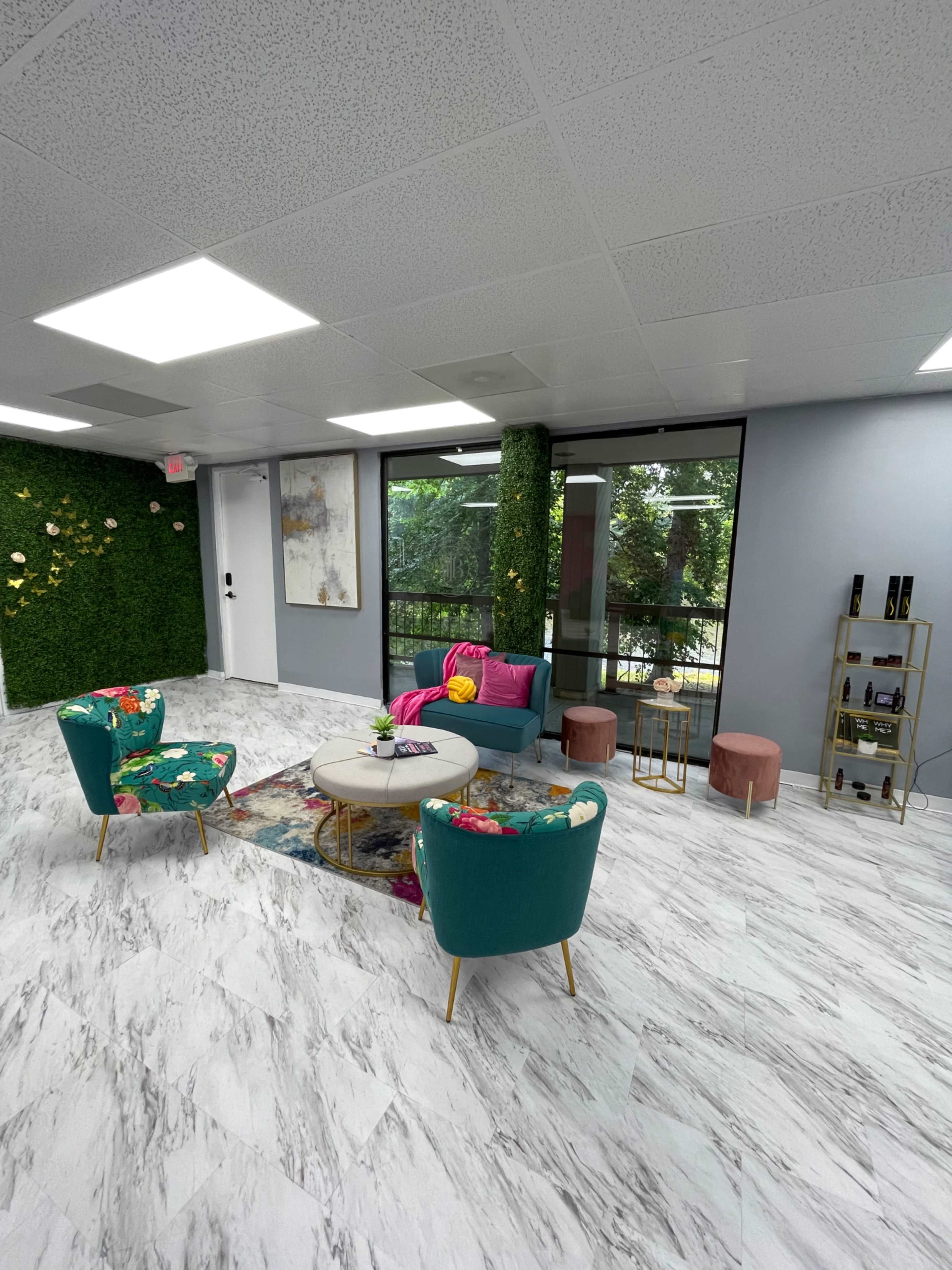 A modern interior space with colorful seating, a circular coffee table, and large windows overlooking greenery.