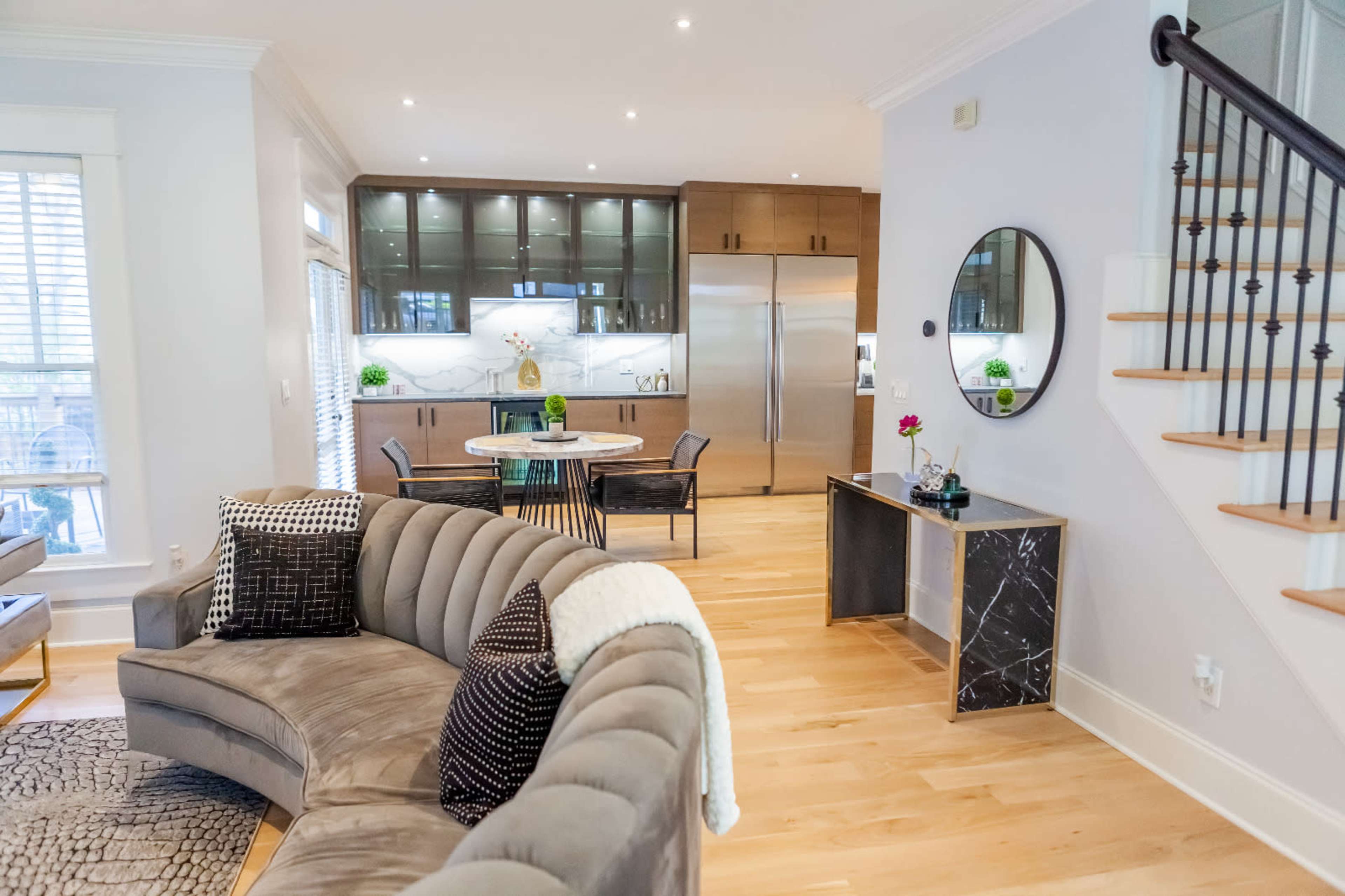 A stylish interior with a circular grey sofa, a dining area in the background, and a small console table near a staircase.