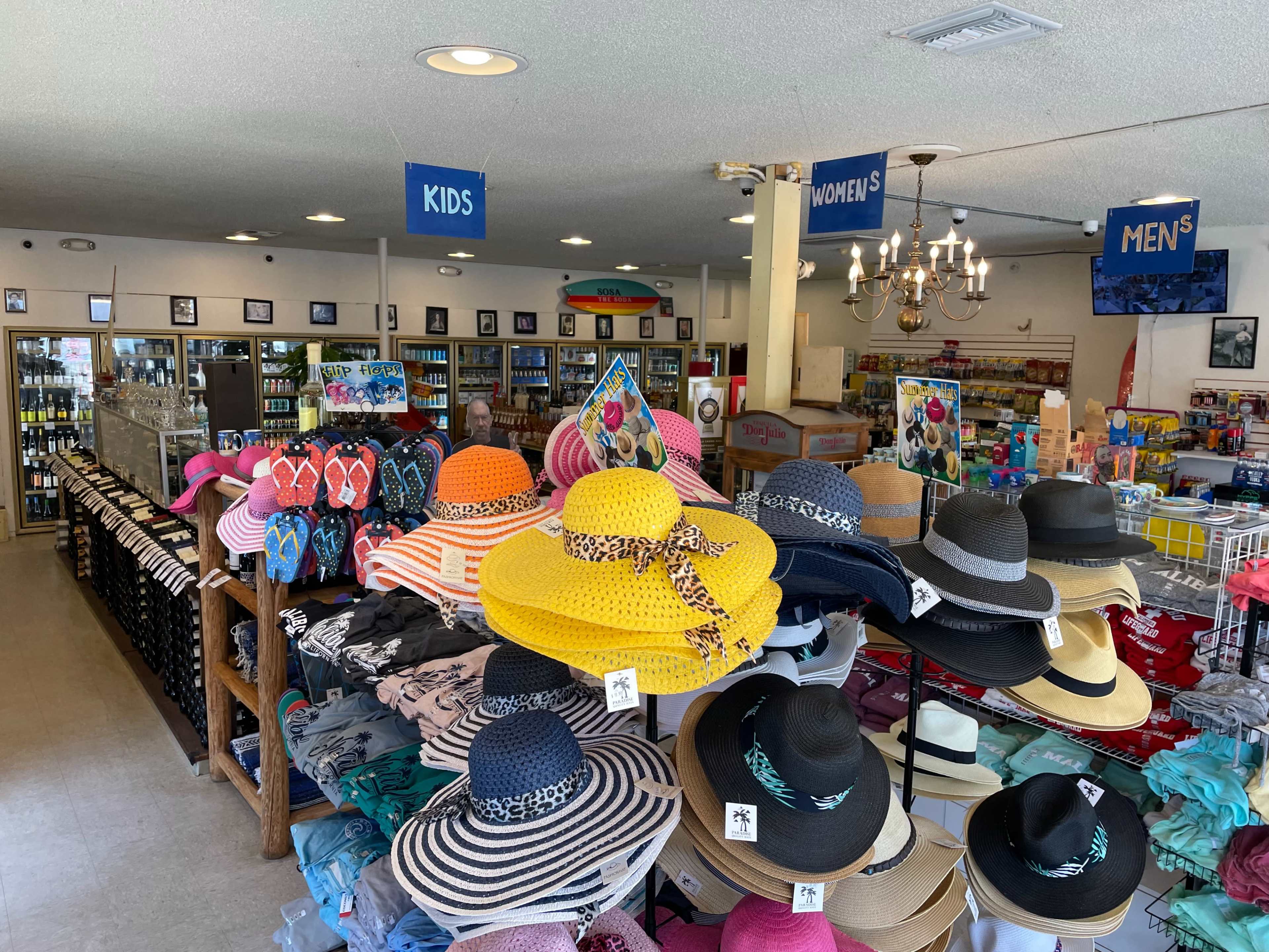 The interior of a retail store features shelves stocked with various hats on display, alongside organized sections for kids, women's, and men's merchandise.