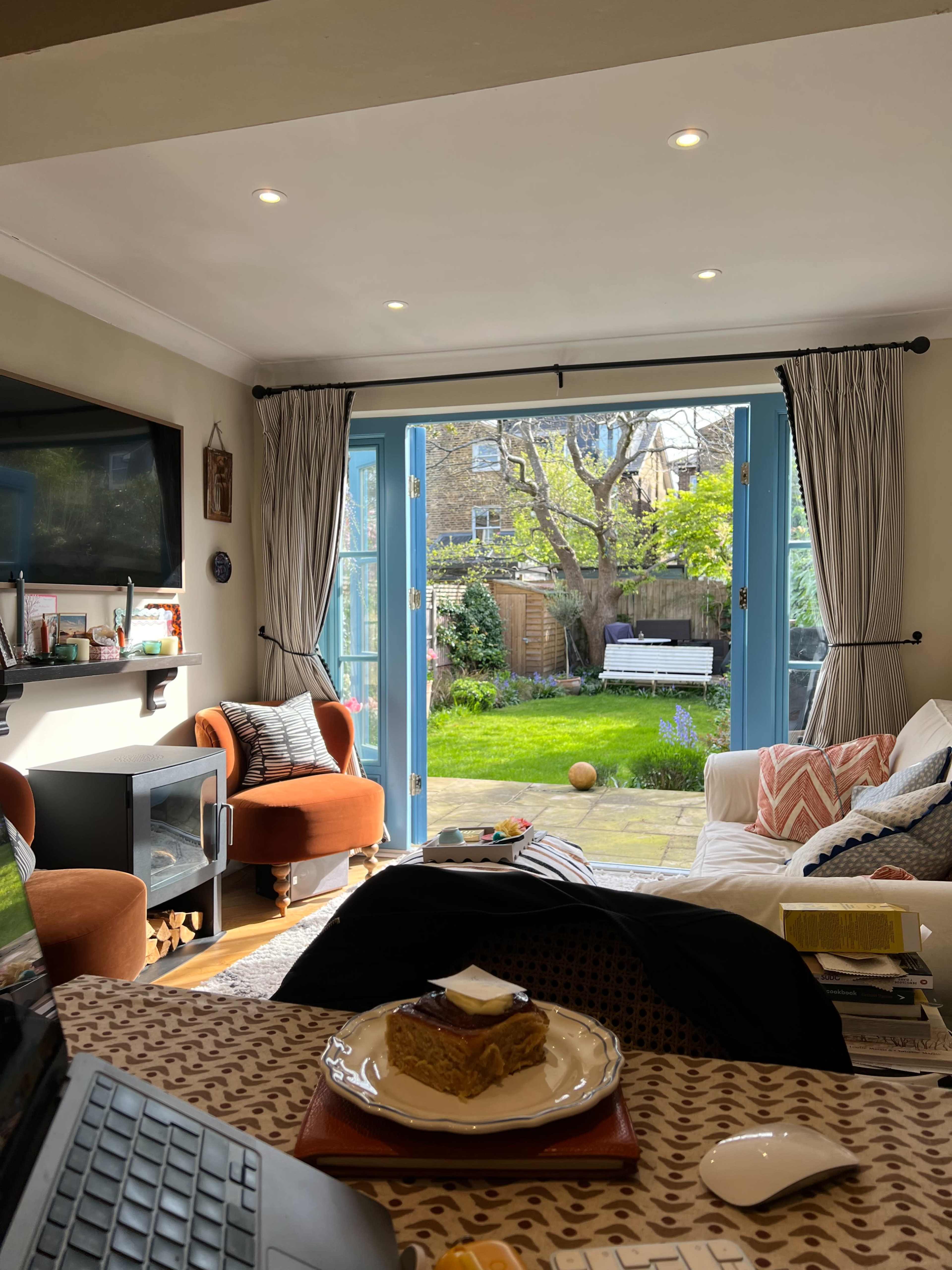 A cozy living room with two orange armchairs, a white couch, and large glass doors opening to a garden with a tree and green grass.