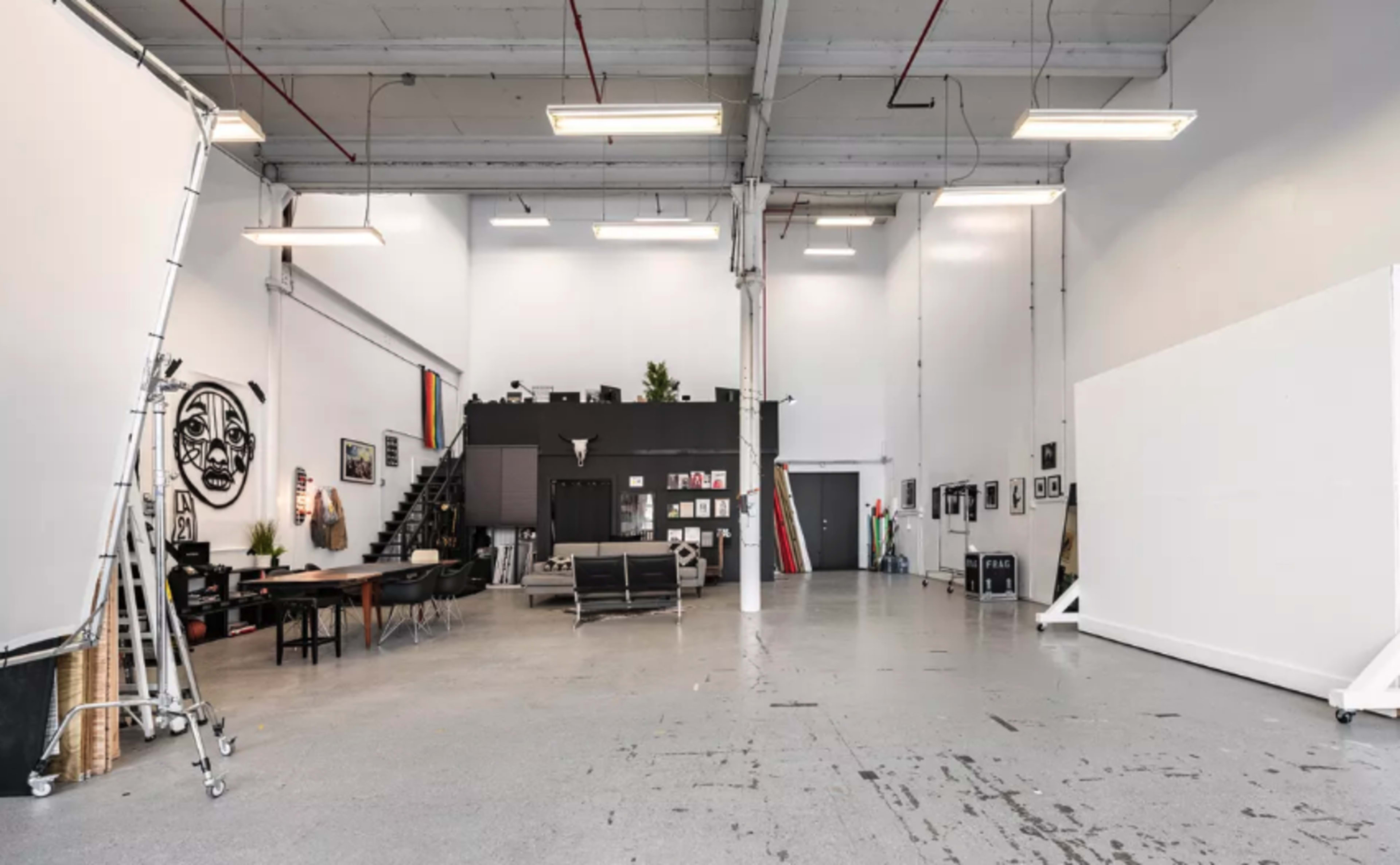 A spacious, well-lit studio with a black feature wall, large white backdrops, and various art pieces and furniture arranged throughout the room.