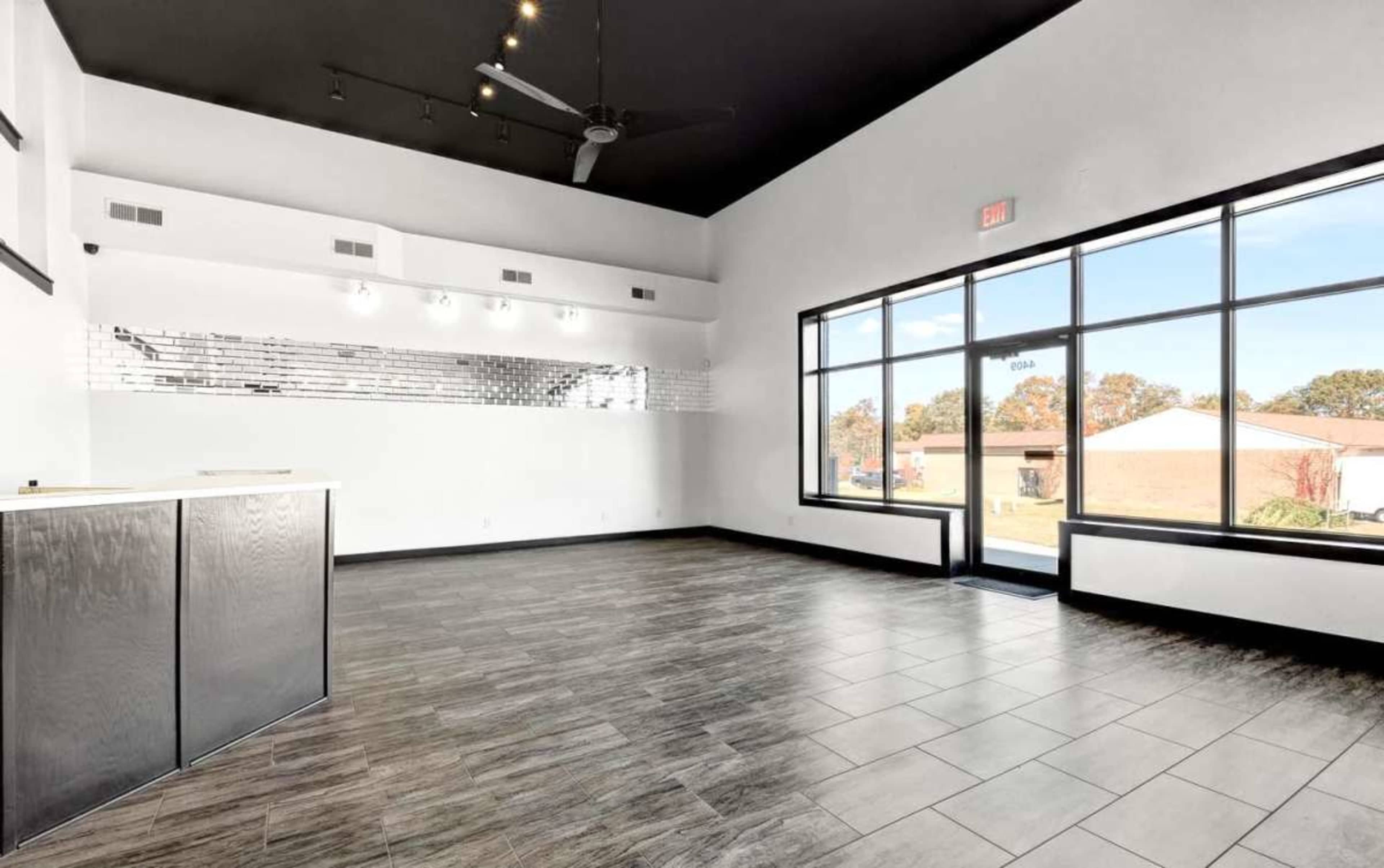 The image depicts an empty, modern interior space with tiled flooring, large windows, and a sleek reception area.