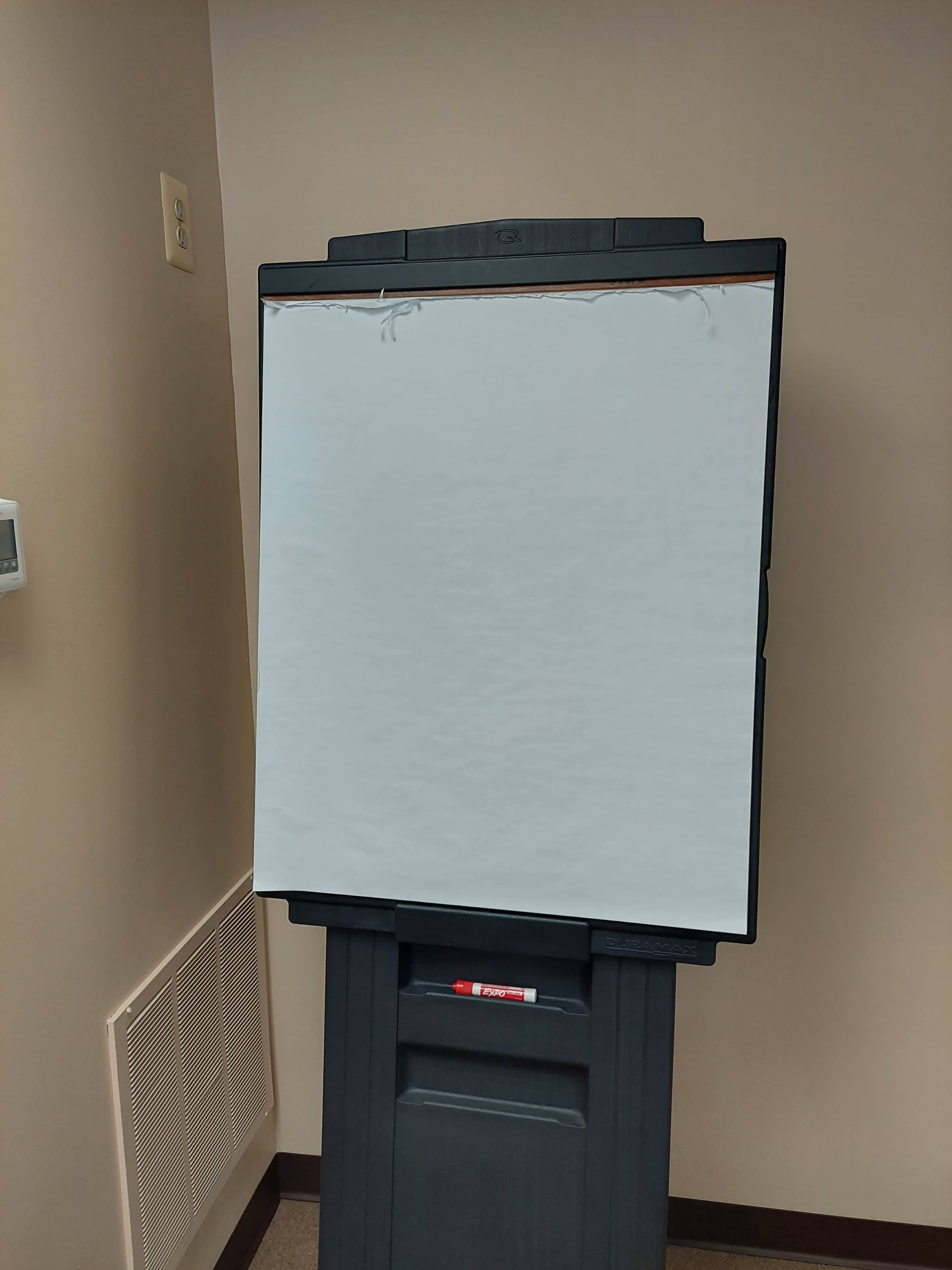 A blank flip chart is mounted on a black easel in a room with beige walls.