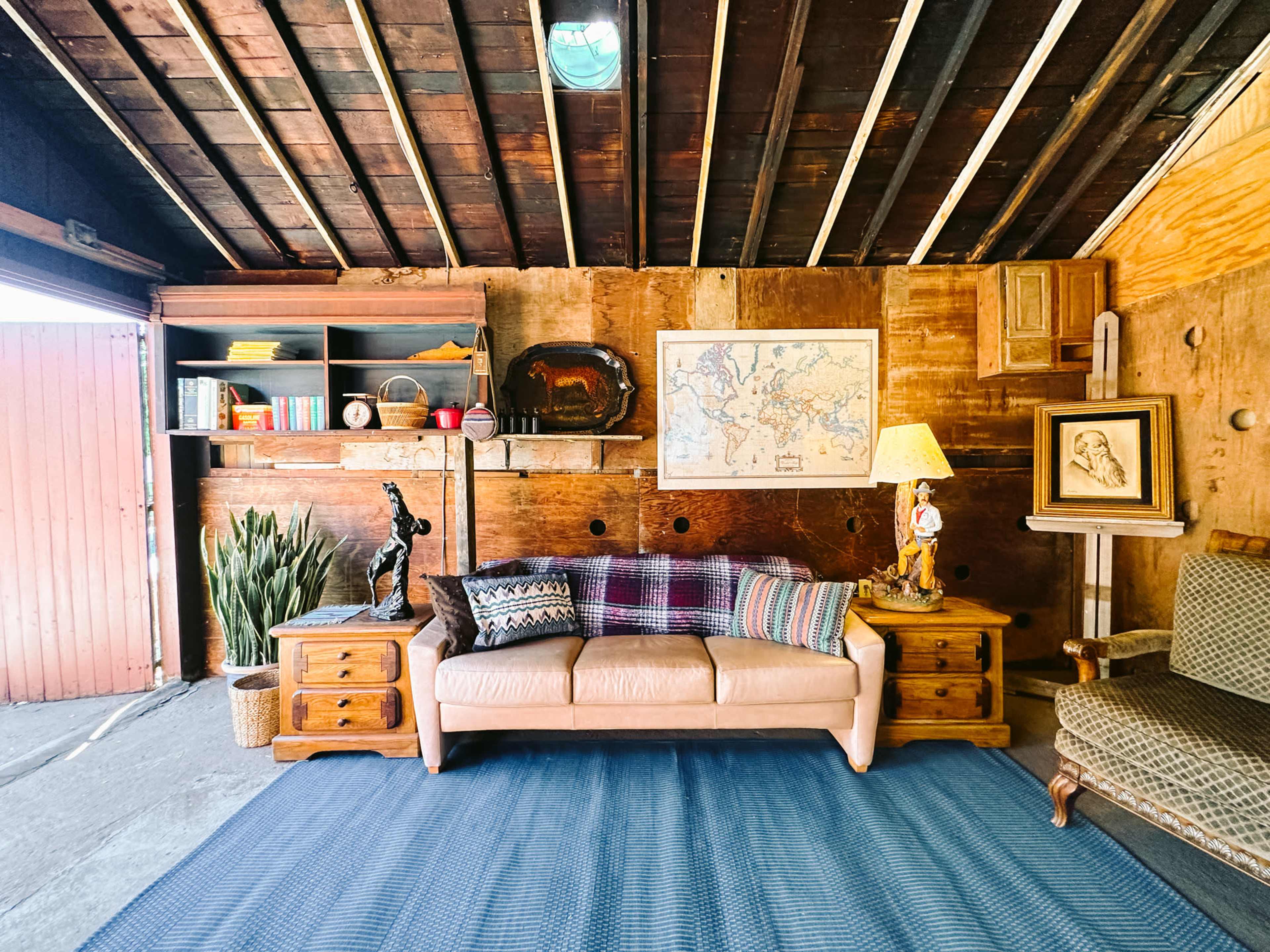 A cozy living space featuring a beige sofa, wooden furniture, a map on the wall, and a plant, set within a rustic wooden interior.