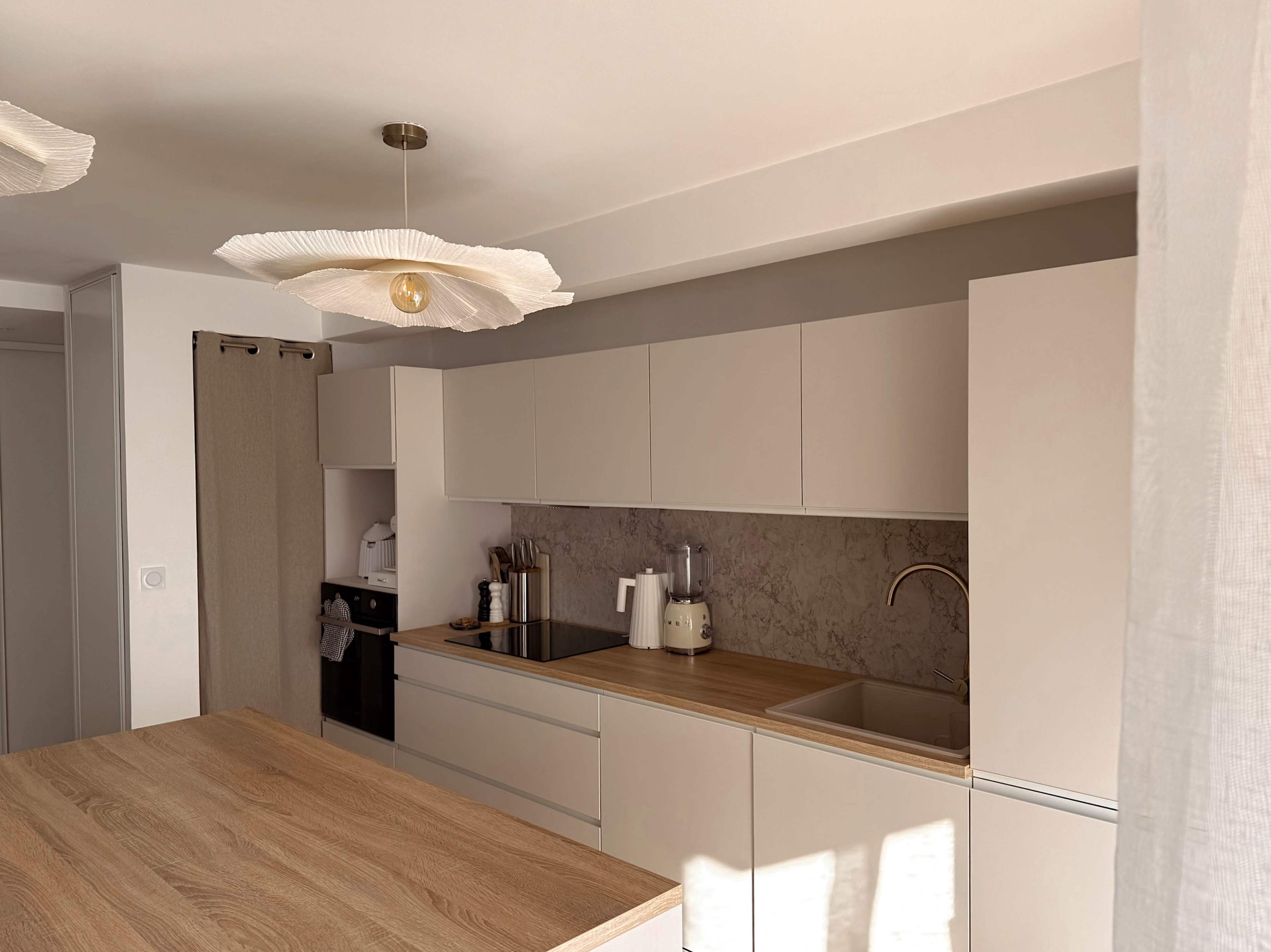 The image shows a modern kitchen with light cabinetry, a wooden island, and a minimalistic design featuring a marble backsplash.