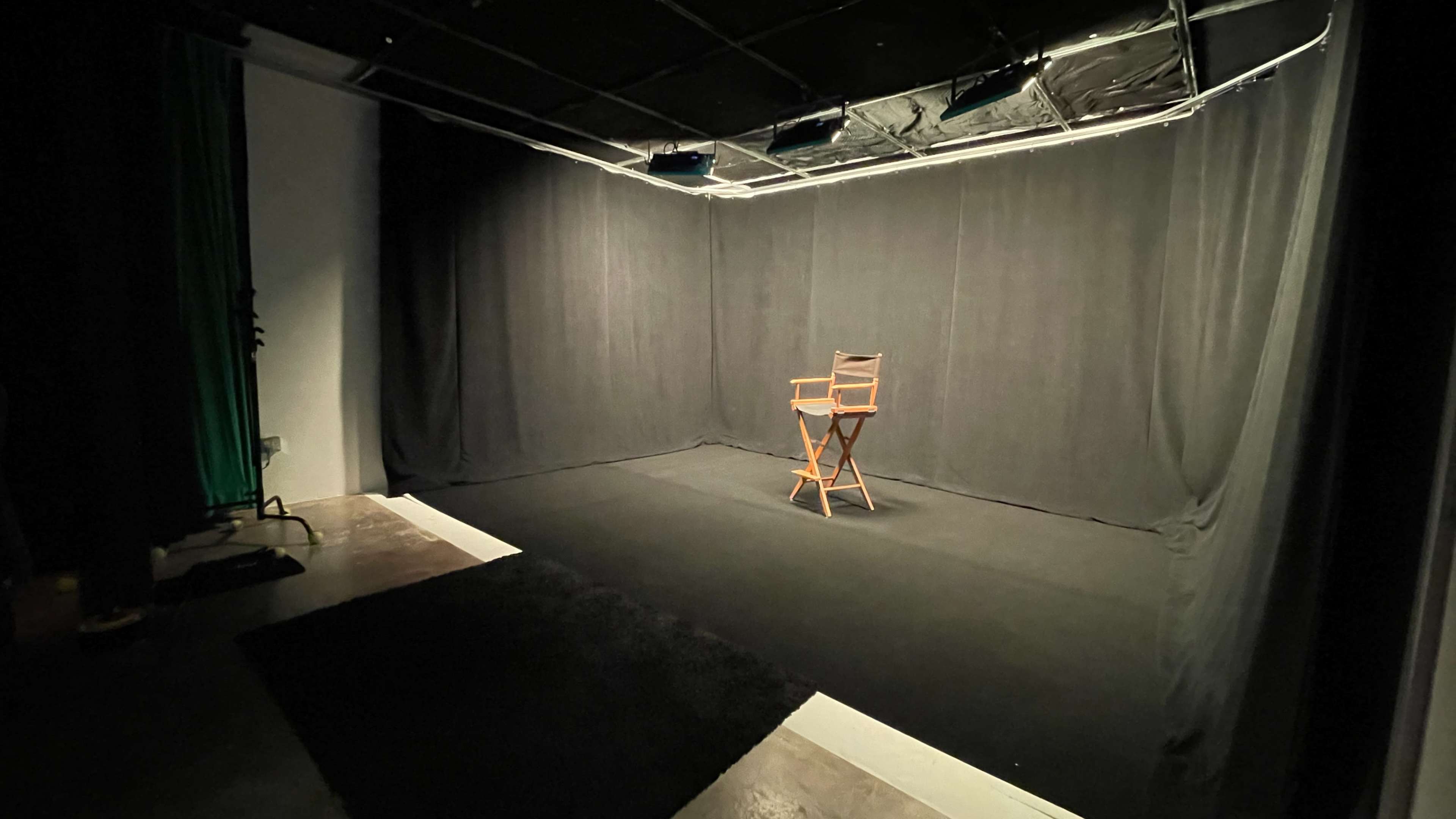 A wooden director's chair is positioned in the center of a dimly lit studio space with black curtains.