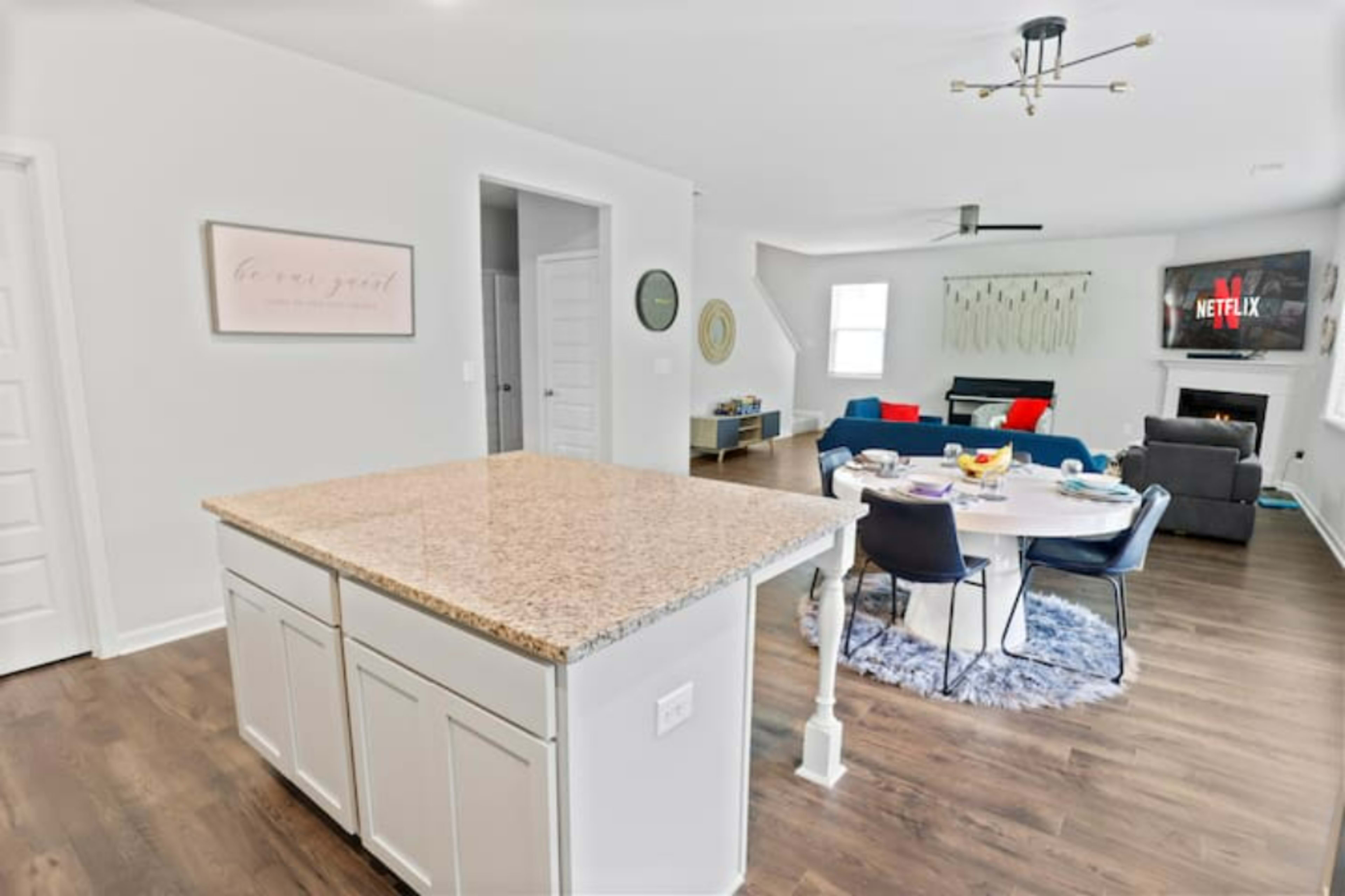 A modern open-concept living space featuring a kitchen island with a granite countertop and a cozy seating area with a couch, coffee table, and a television in the background.