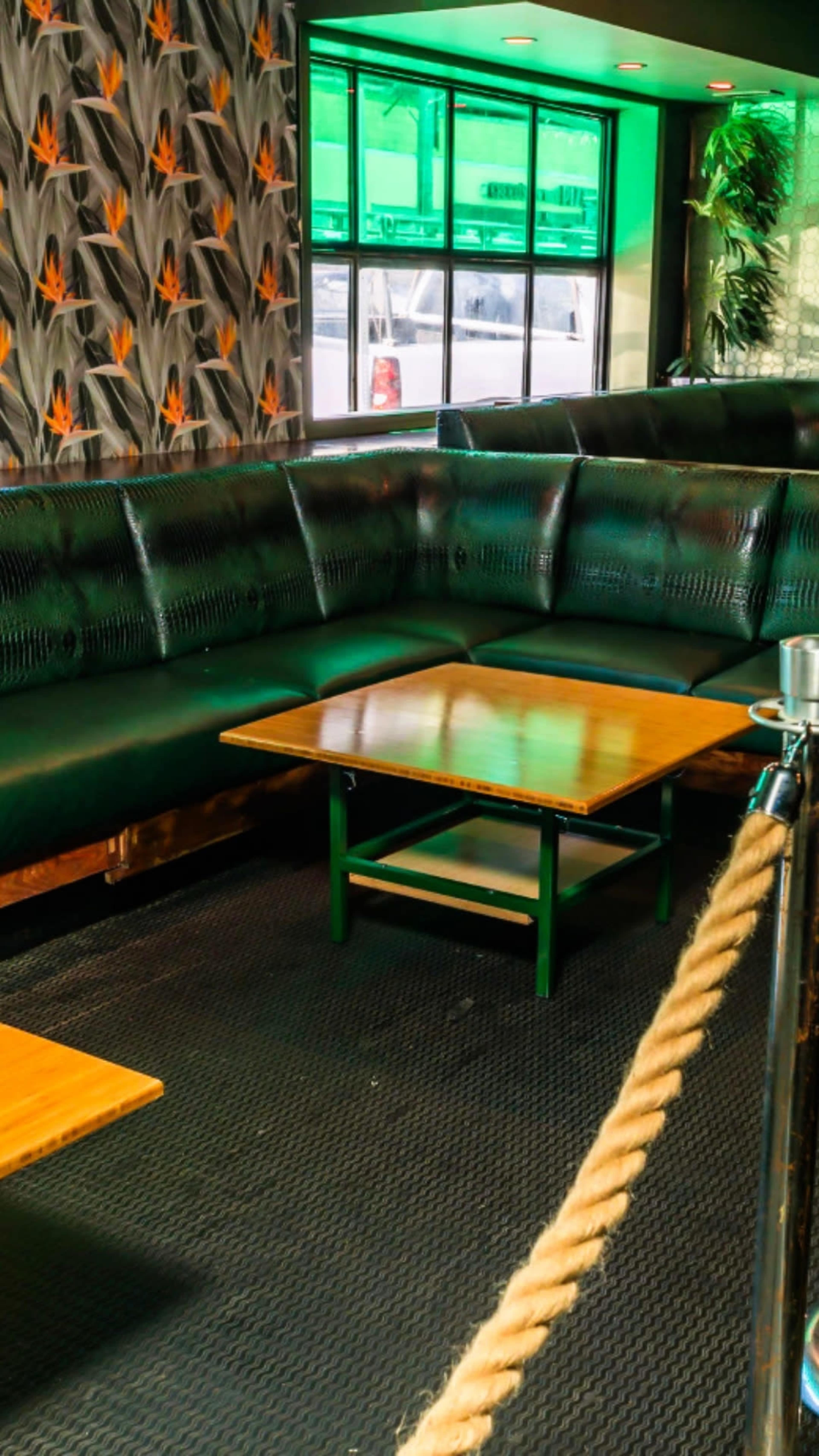 A seating area with a green leather couch, wooden tables, and a rope barrier under a window with a view of the street.