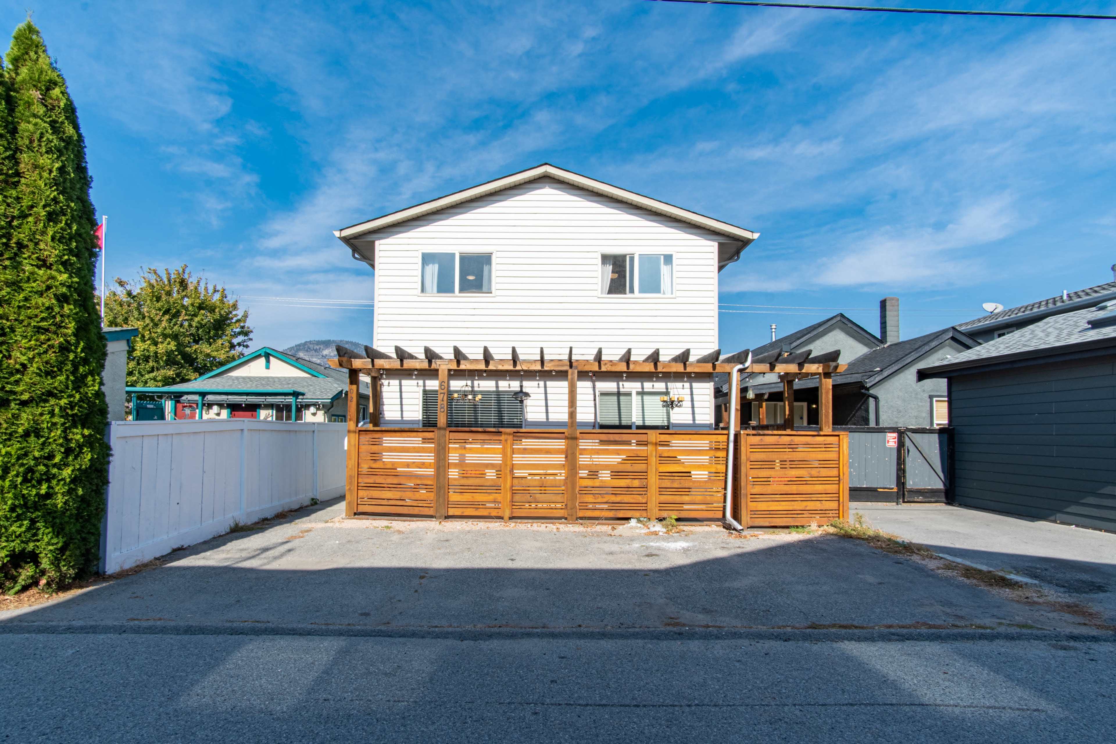 A two-story white building with a wooden pergola in front, surrounded by fences and neighboring houses.