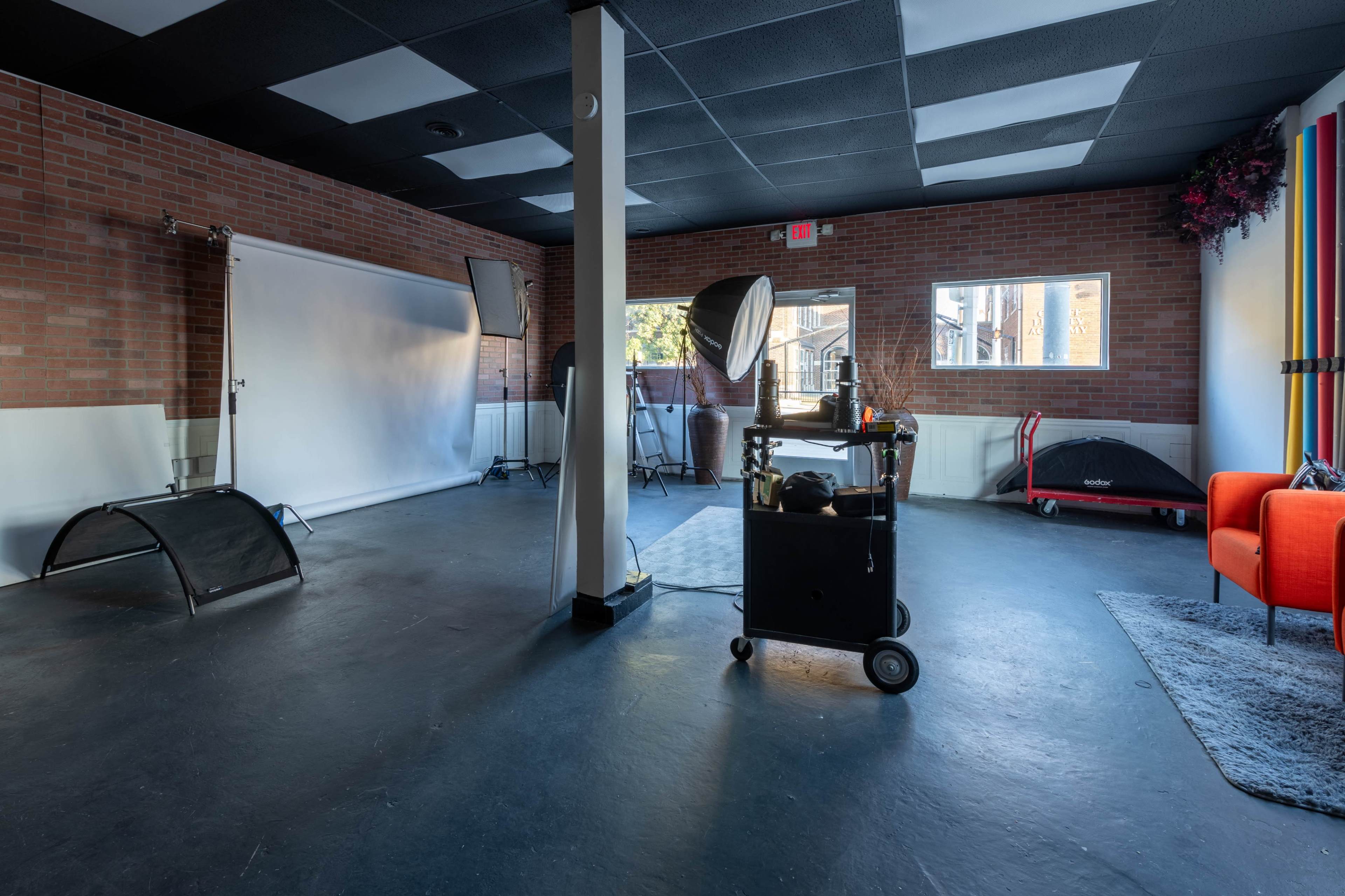 A spacious photography studio with soft lighting equipment, a backdrop stand, and colorful decorations against brick walls.