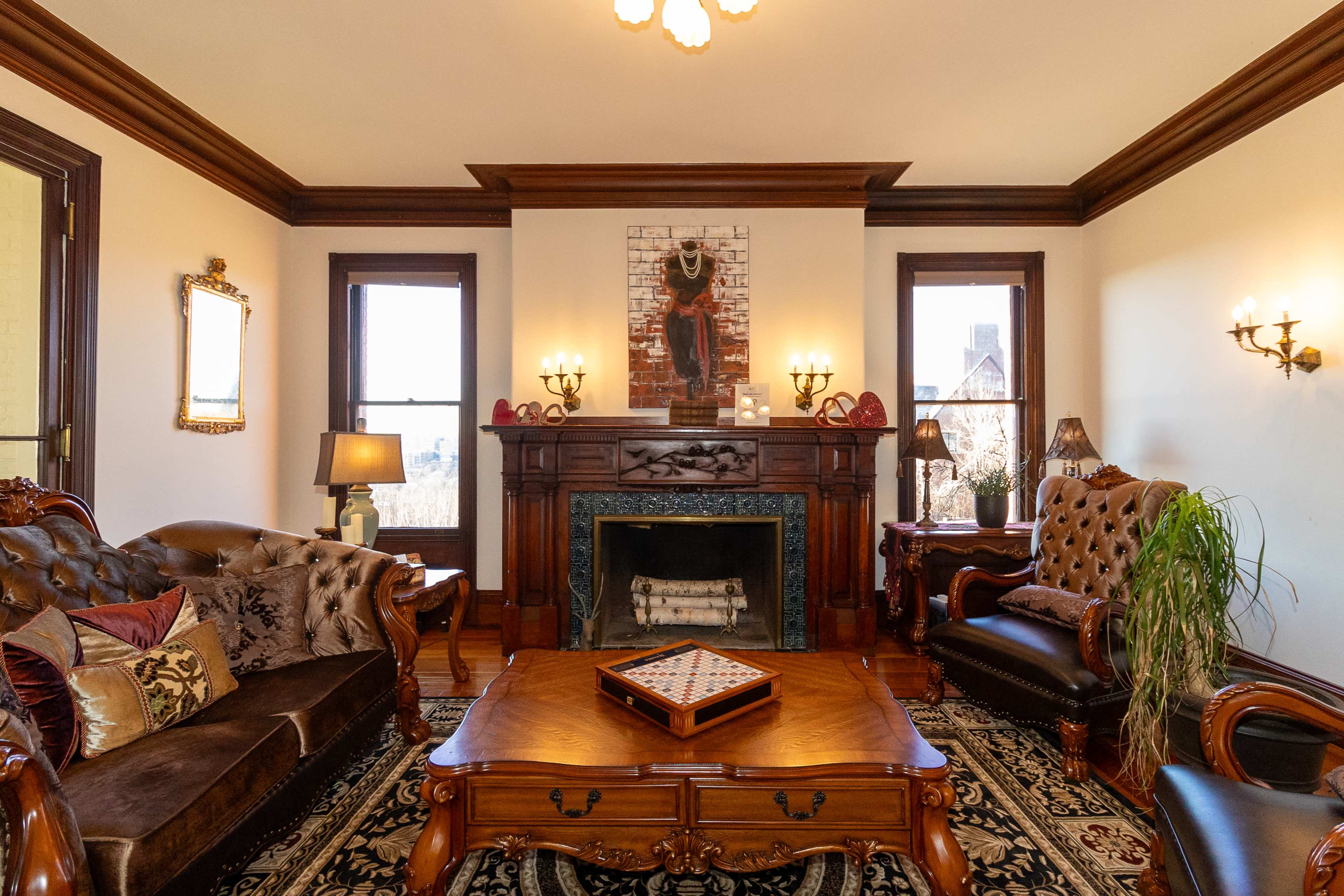 The living room features ornate wooden furniture, a decorative fireplace, and two windows illuminating the space.