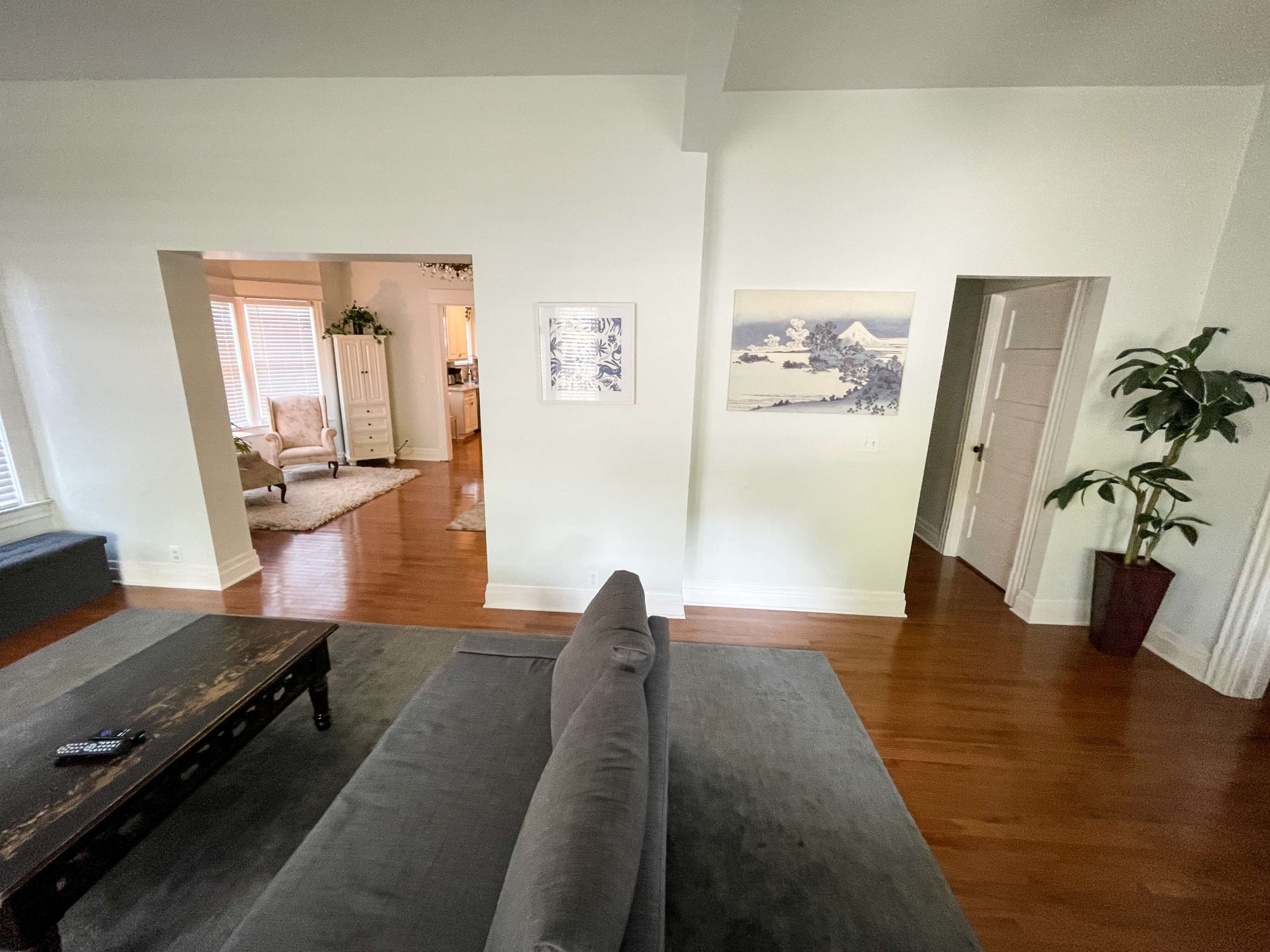 The image shows a light-filled living room with a gray sofa, a wooden coffee table, and an open doorway leading to another room.