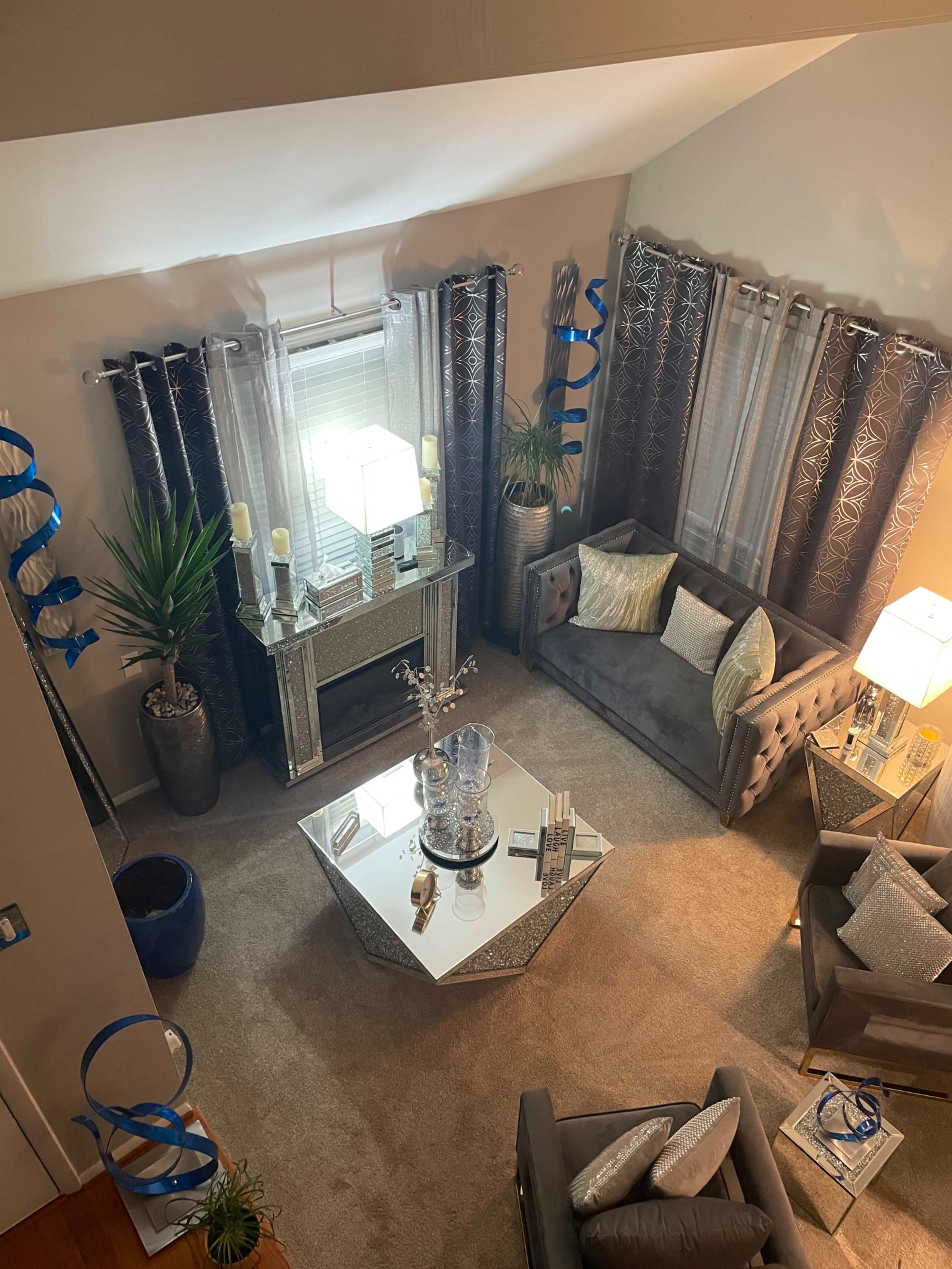 A modern living room with gray furniture, decorative plants, and shimmering light fixtures while blue streamers hang along the walls.