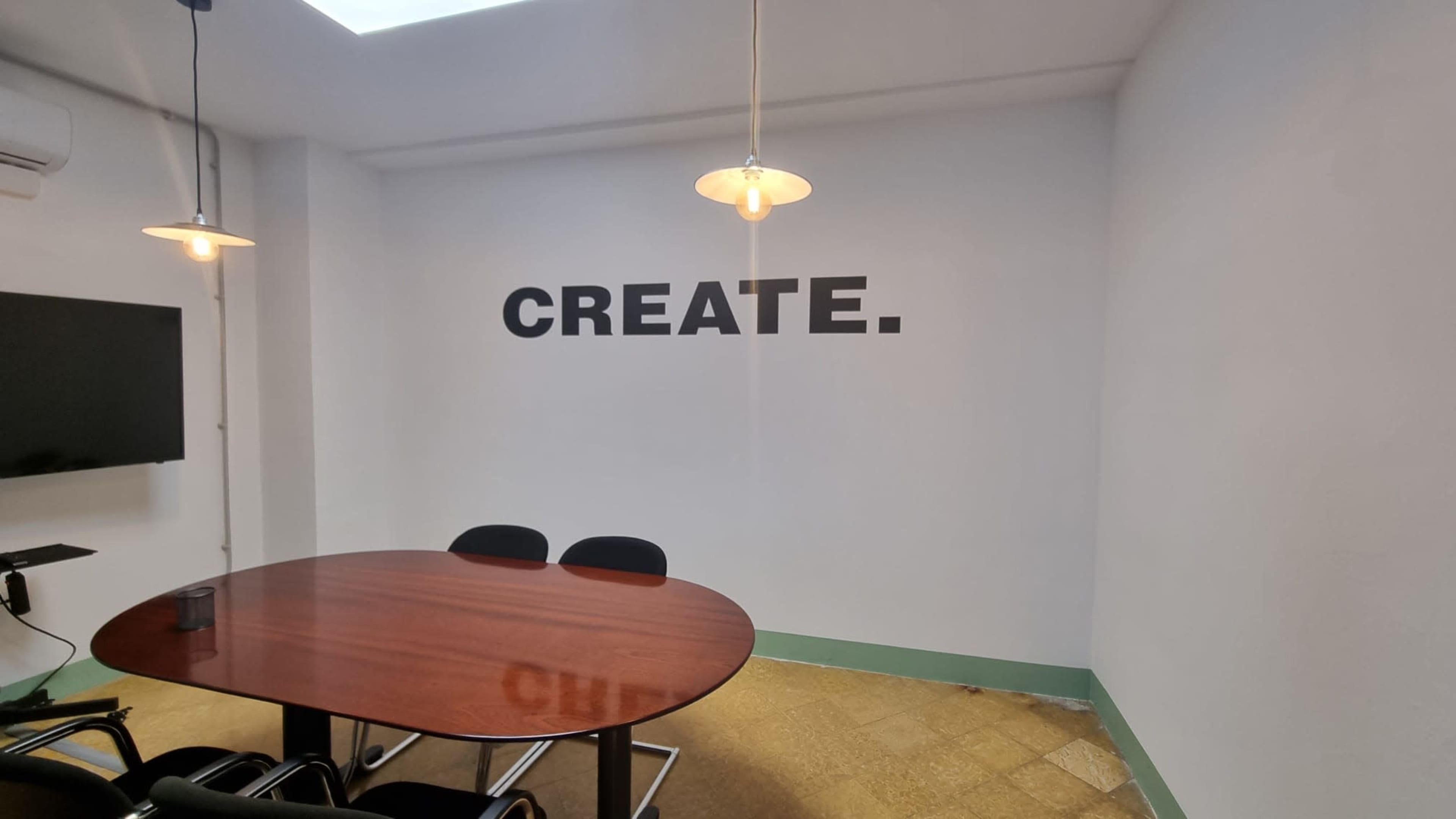 A conference room features a round wooden table and a wall with the word "CREATE." in bold lettering.