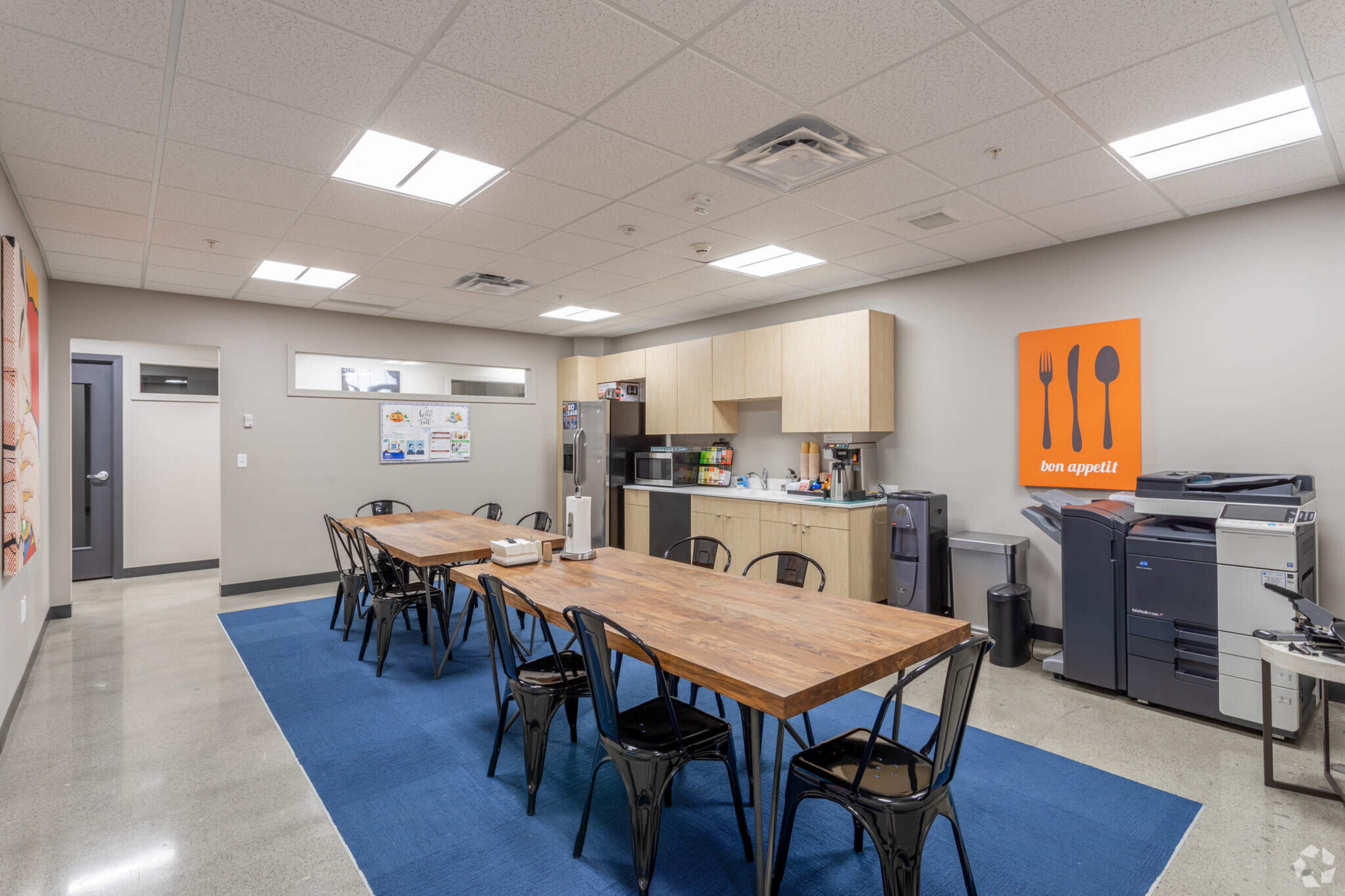 A kitchen and dining area with a long wooden table, black chairs, cabinetry, and various kitchen appliances.