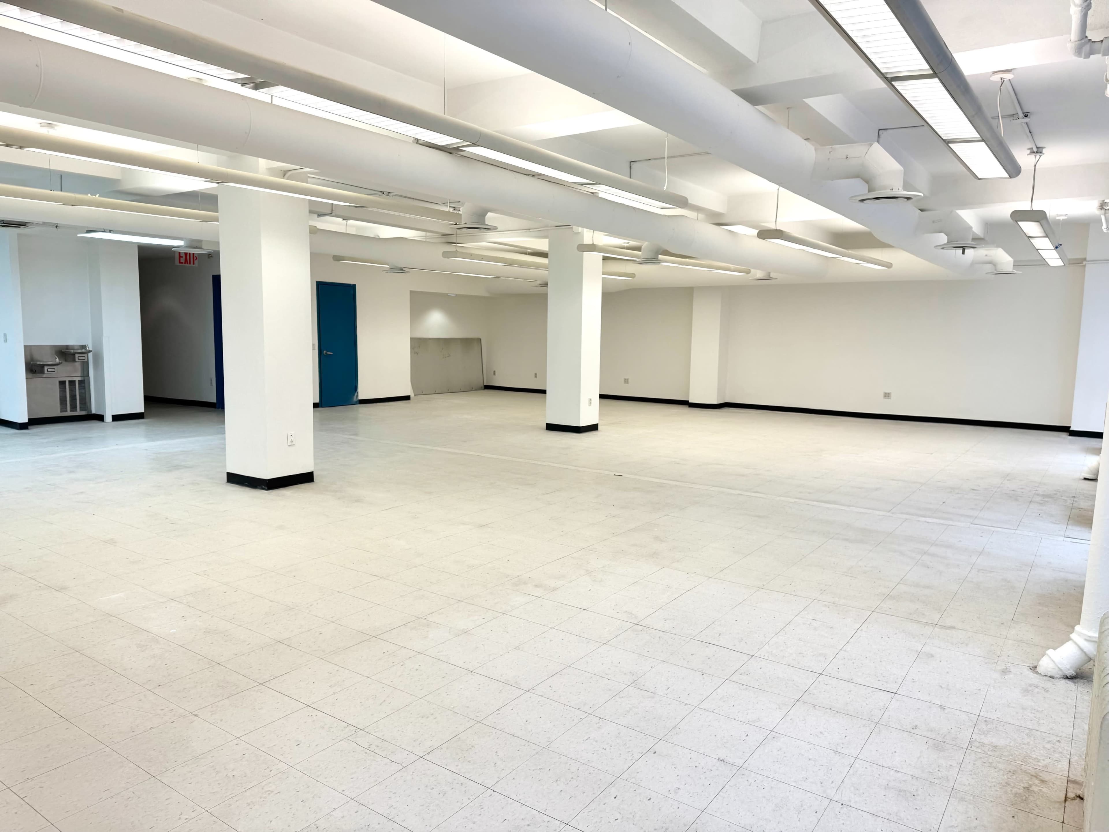 The image shows a spacious, empty room with white walls, tile flooring, and several overhead light fixtures.
