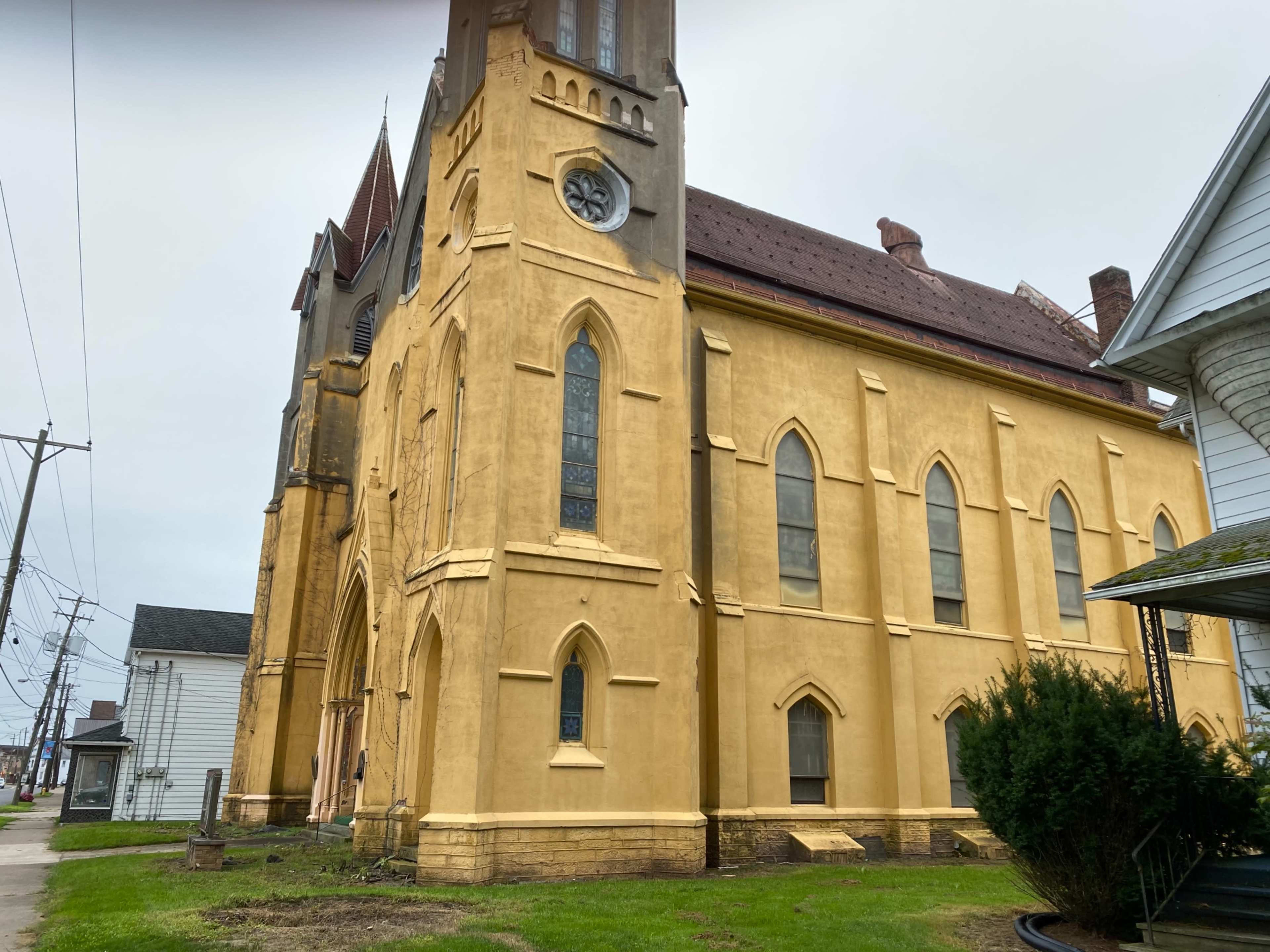 A yellow-stucco church with a clock tower and pointed arches, situated next to residential buildings.