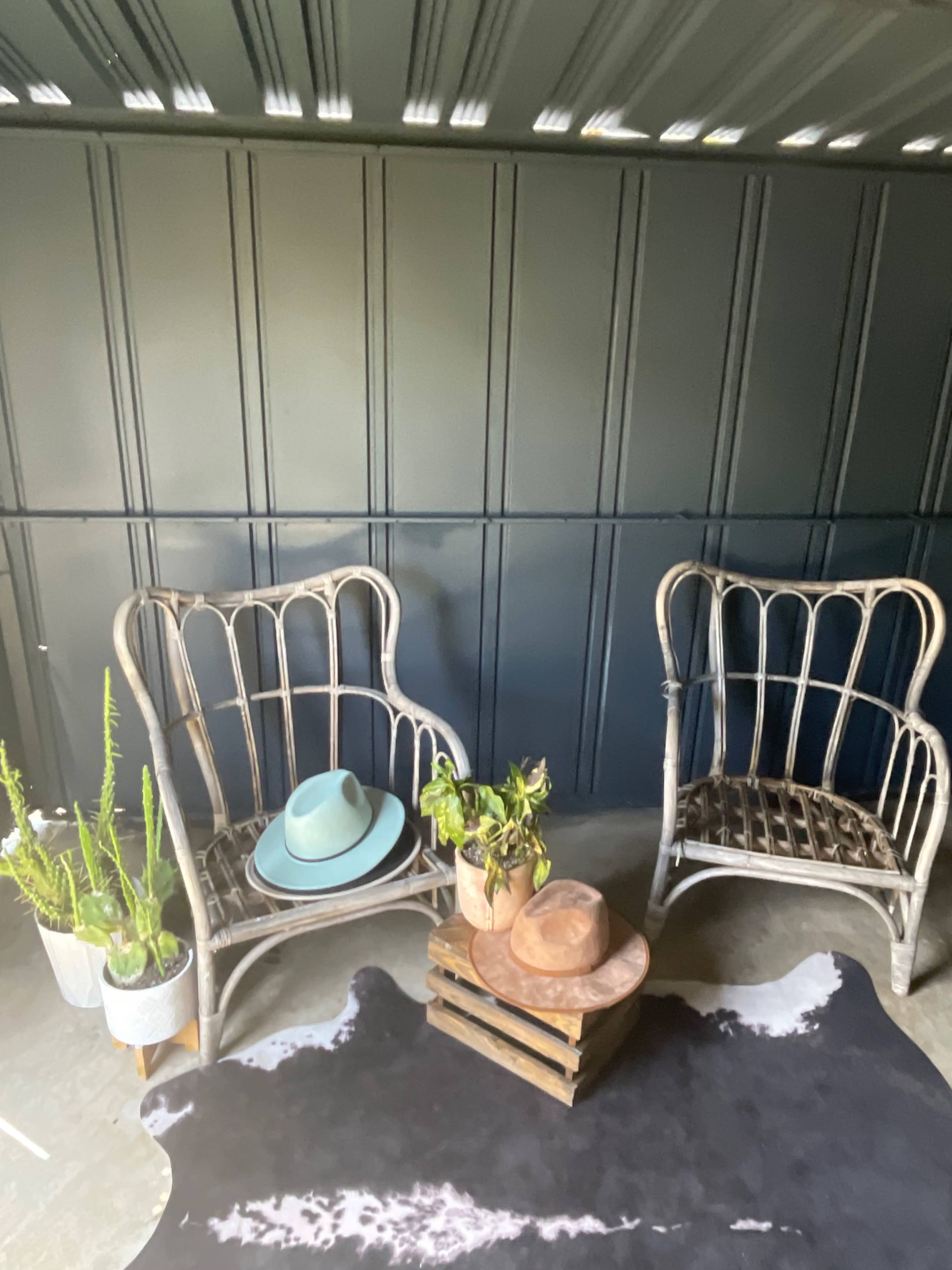 Two vintage-style chairs are positioned on a patterned rug beside a small wooden crate holding several hats and potted plants.