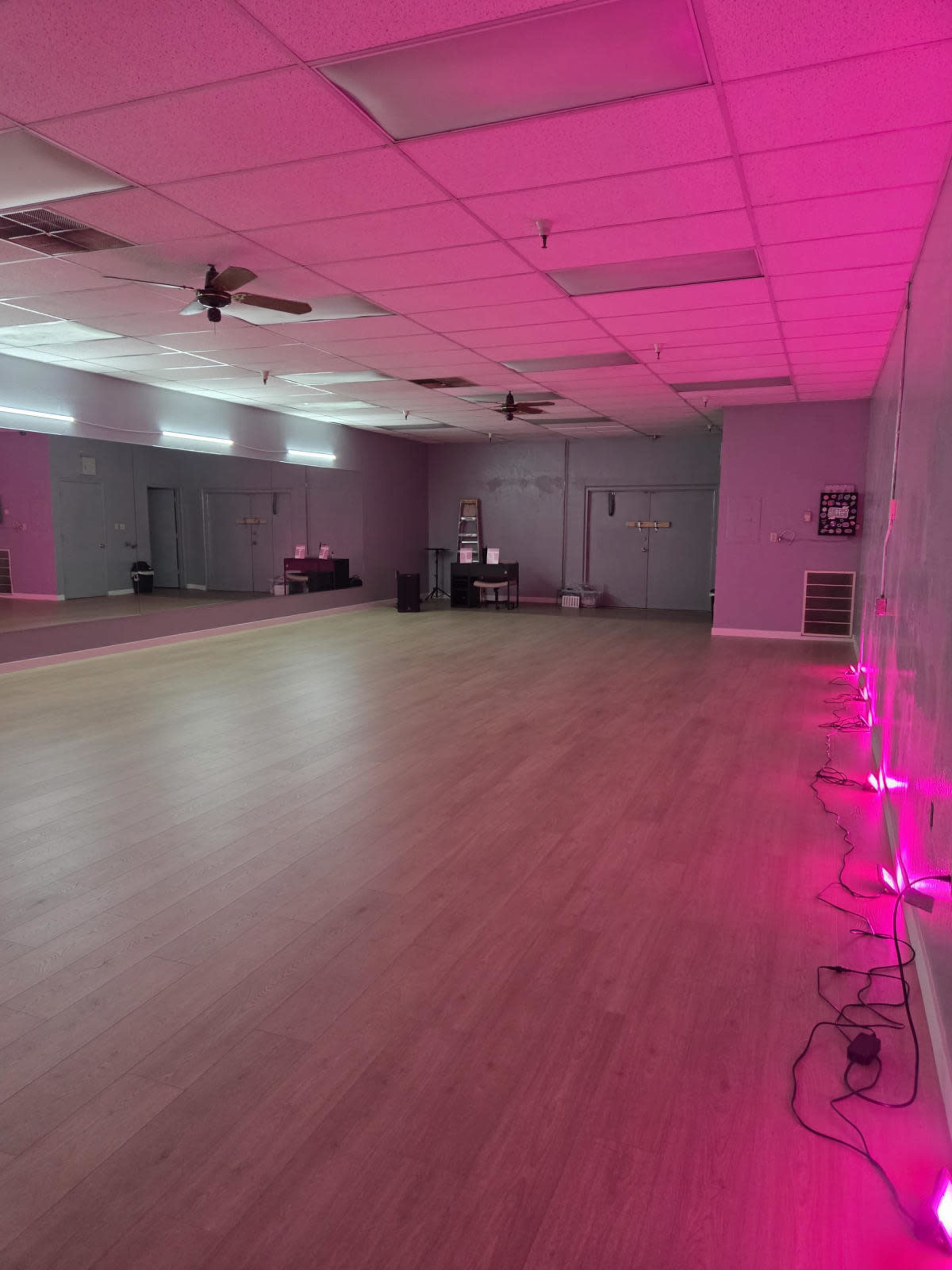 The image shows an empty dance studio with pink LED lights along the walls and large mirrors reflecting a spacious wooden floor.