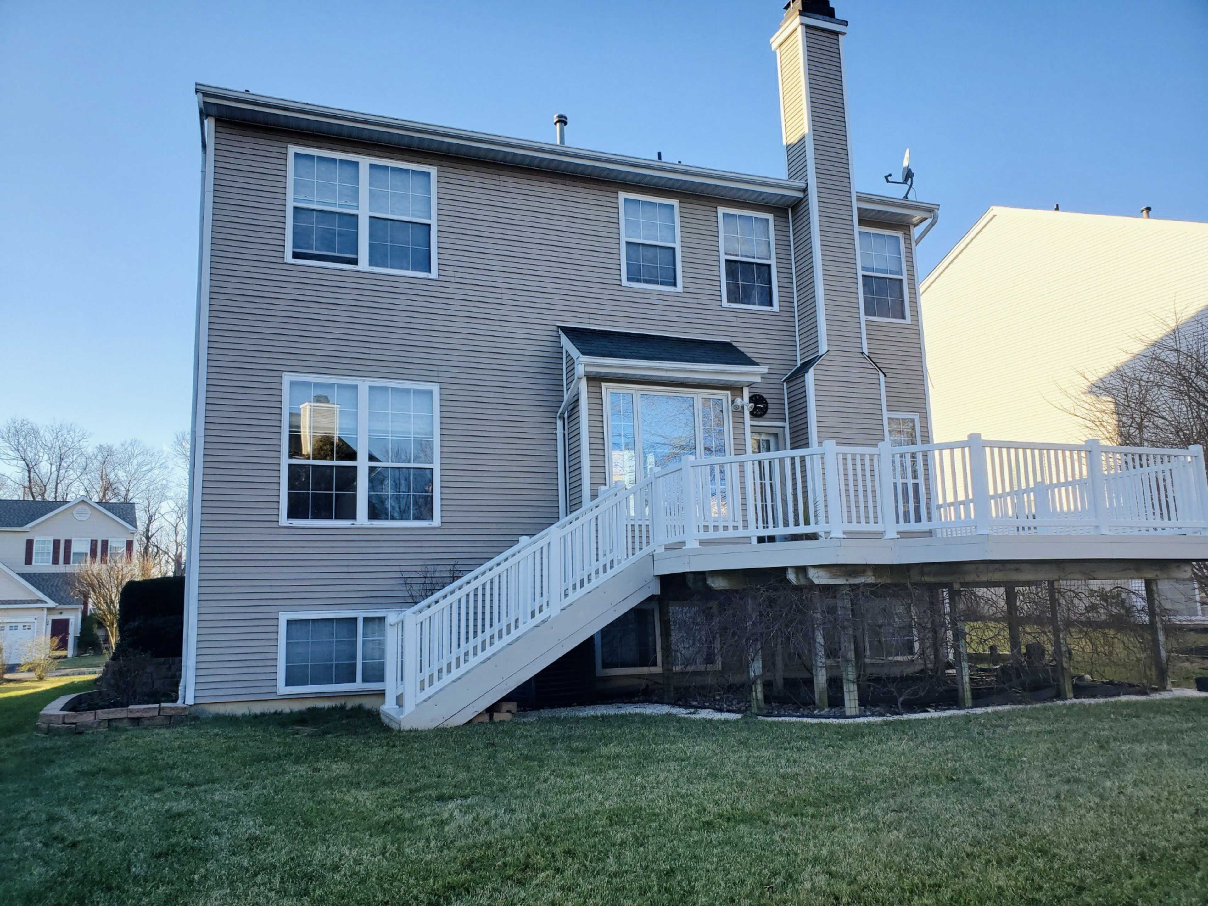 A three-story house with beige siding and a white deck on the back.