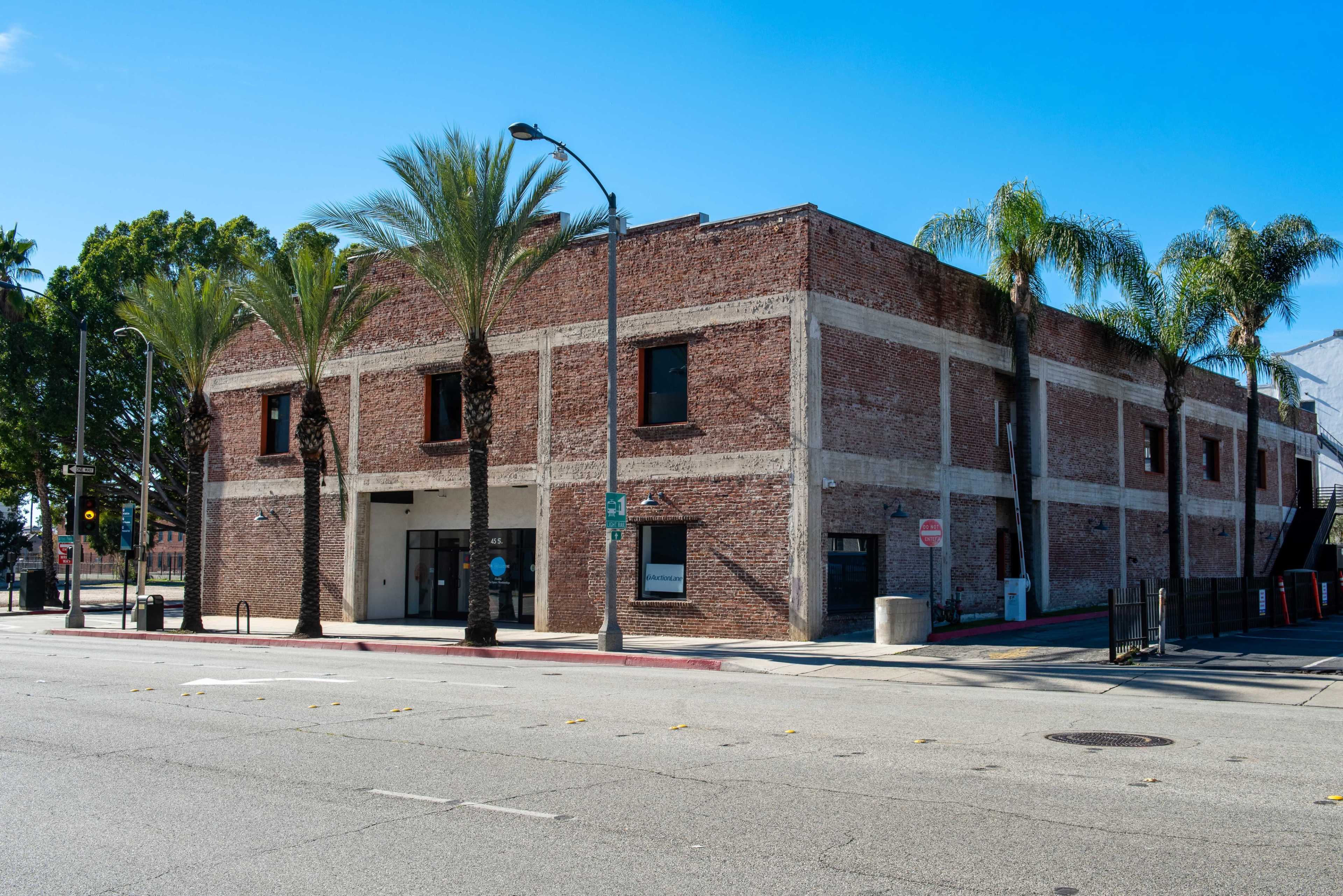A two-story brick building with palm trees in front sits on a street corner.