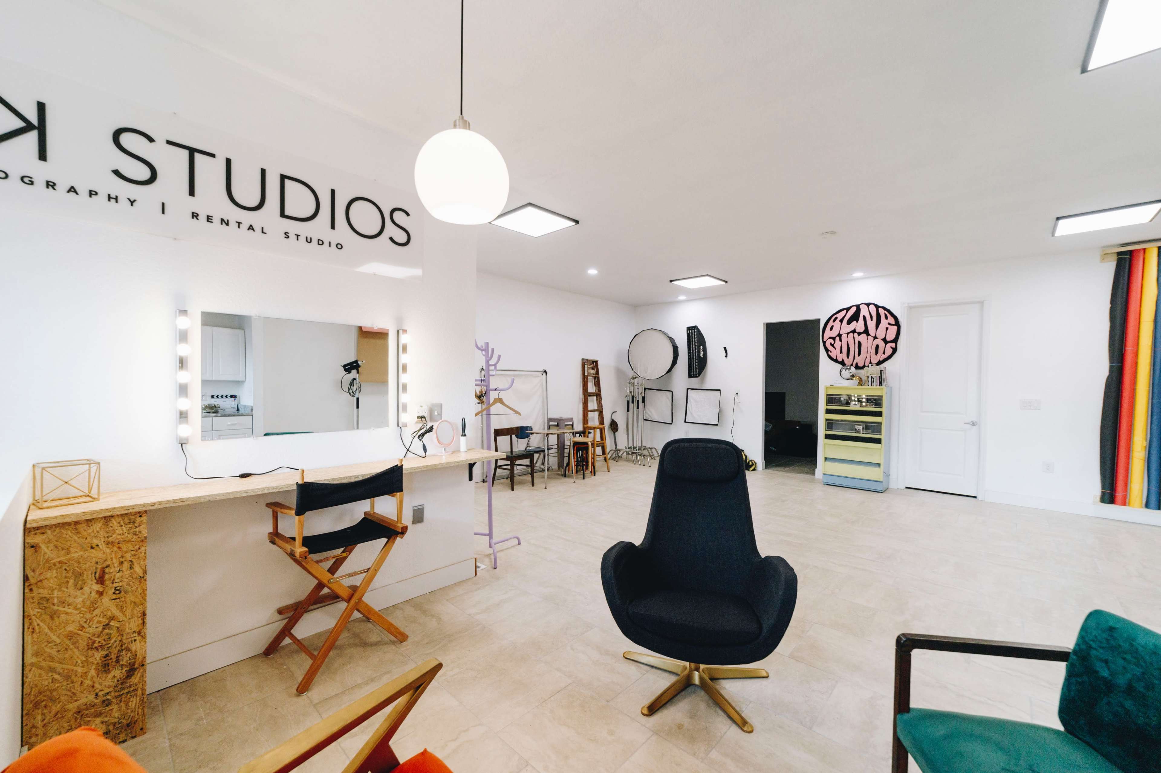 The image shows the interior of a photography and rental studio, featuring a large mirrored vanity, various wall-mounted and freestanding mirrors, and modern seating arrangements.