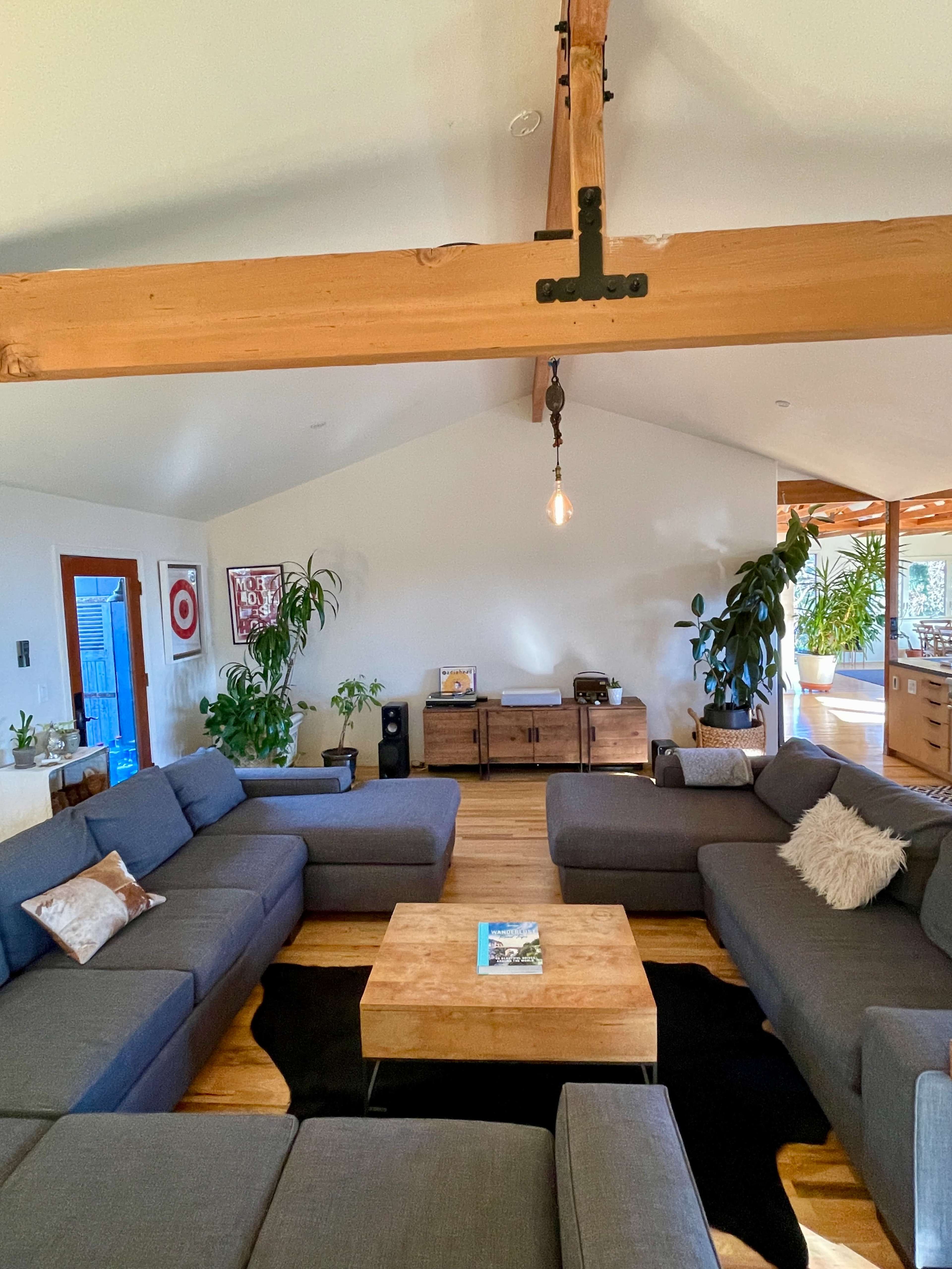 A spacious living room features a large sectional sofa arranged around a wooden coffee table, with plants and wooden furniture enhancing the decor.