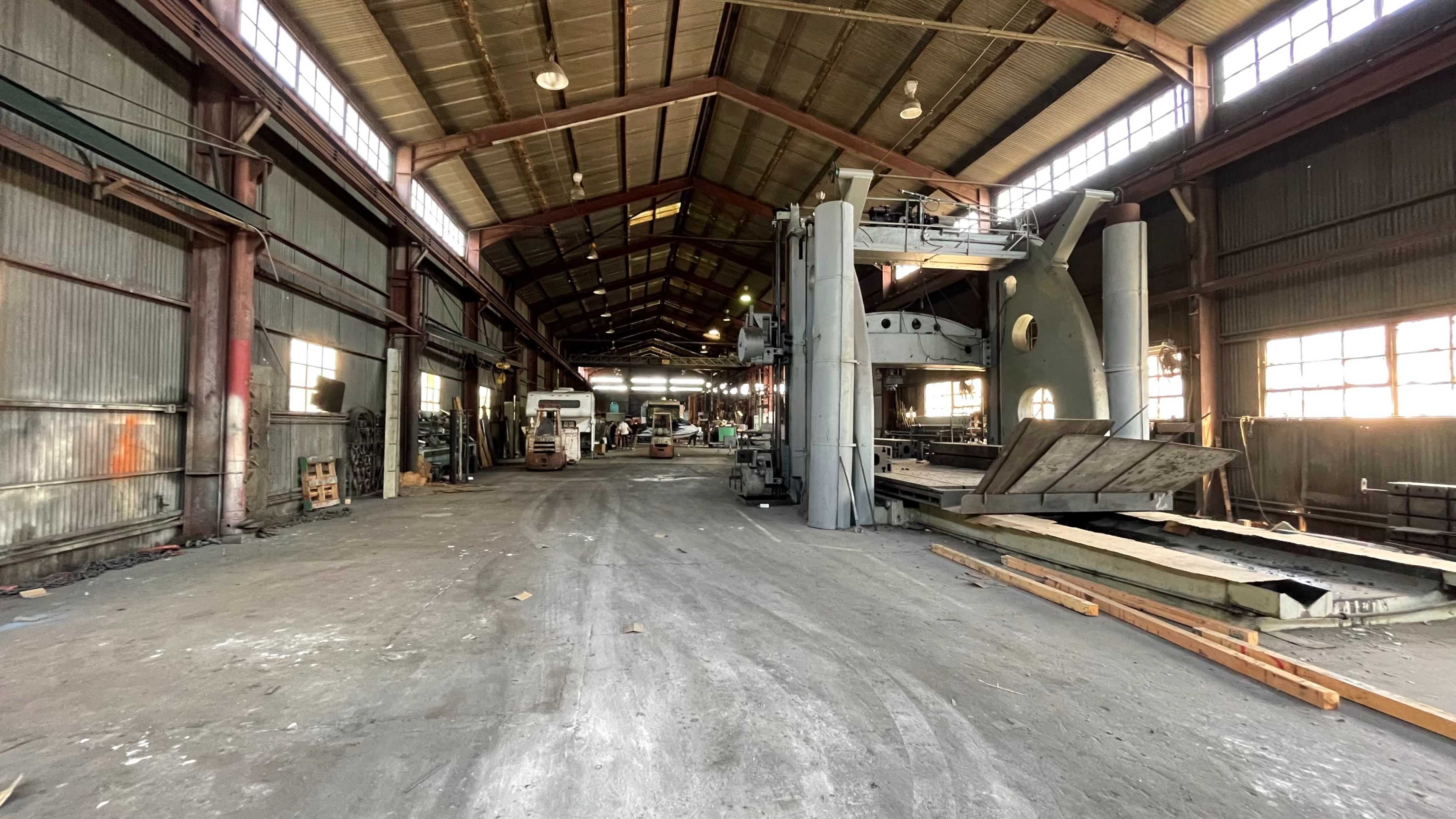 The image shows the interior of a large, industrial warehouse with machinery and equipment scattered throughout.