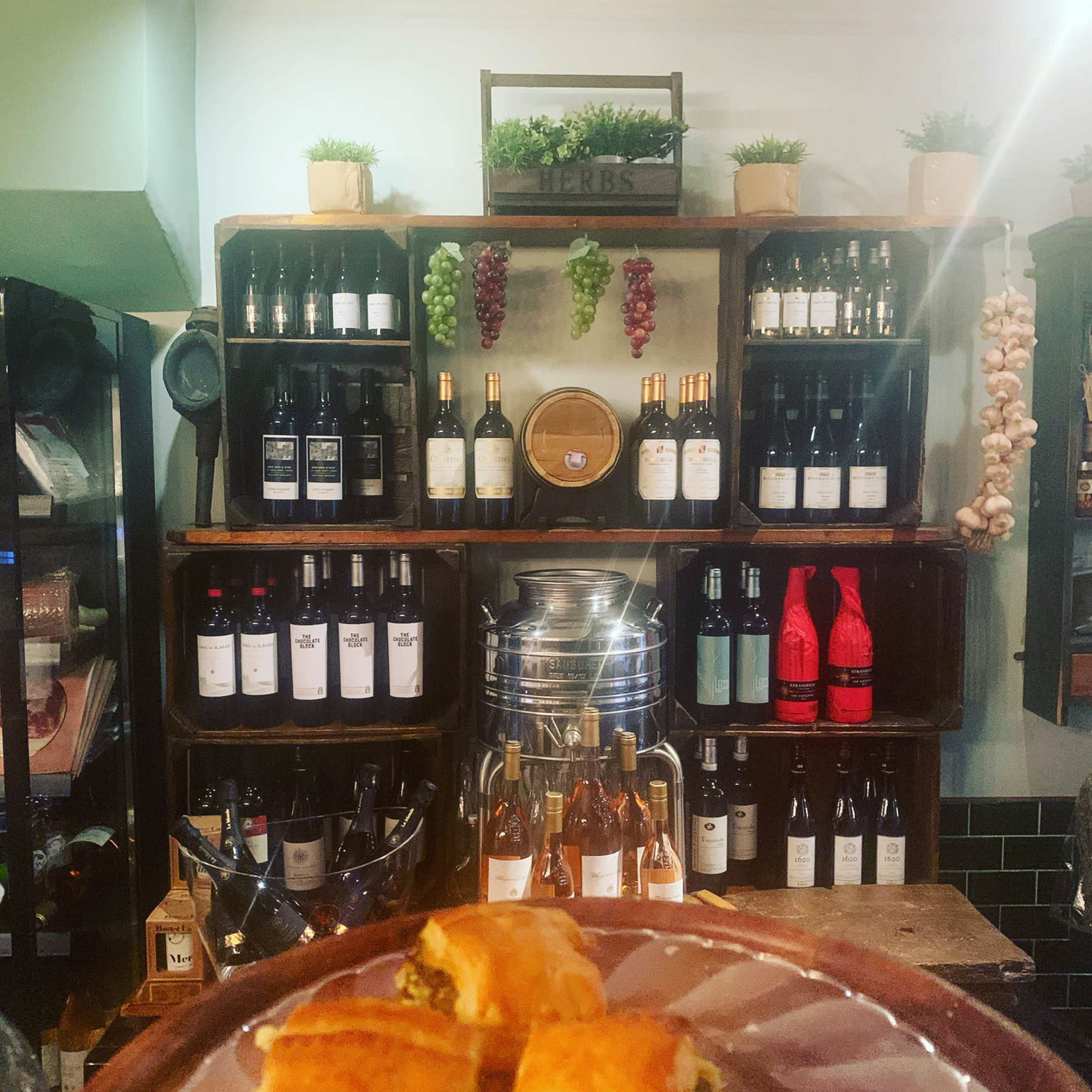 A wooden shelf displays various bottles of wine and decorative plants in a rustic setting.