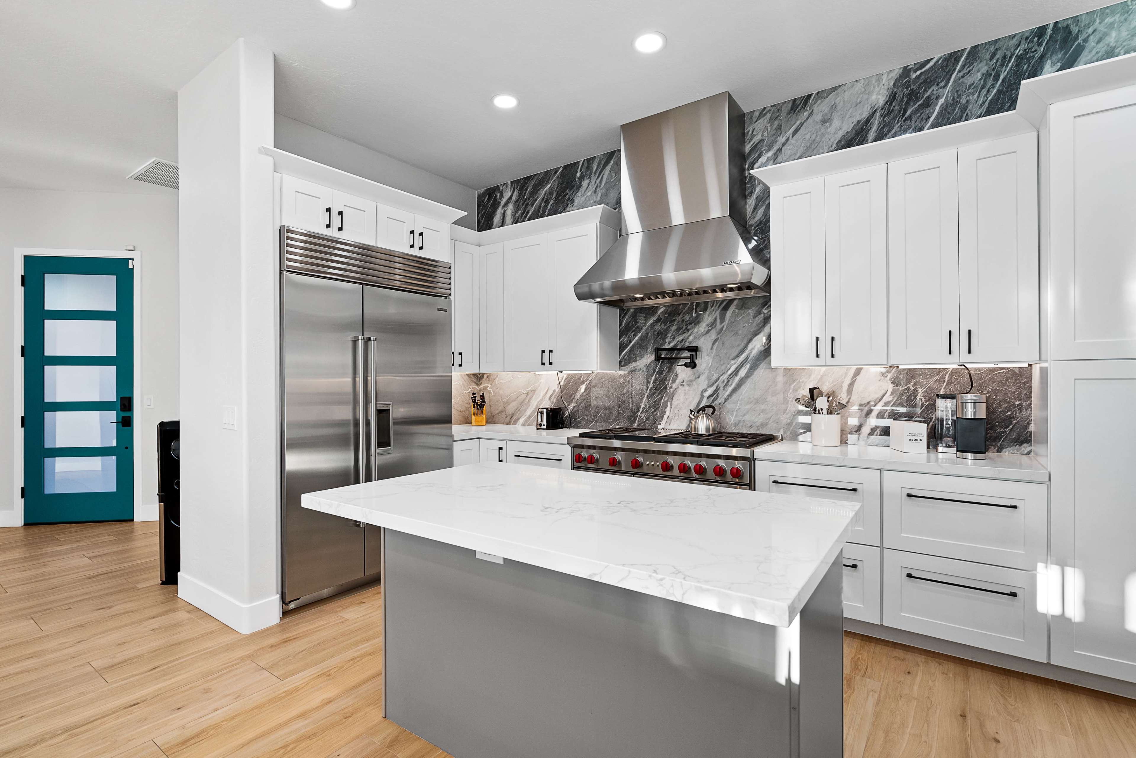 A modern kitchen features stainless steel appliances, white cabinetry, and a large marble island with a contrasting gray base.
