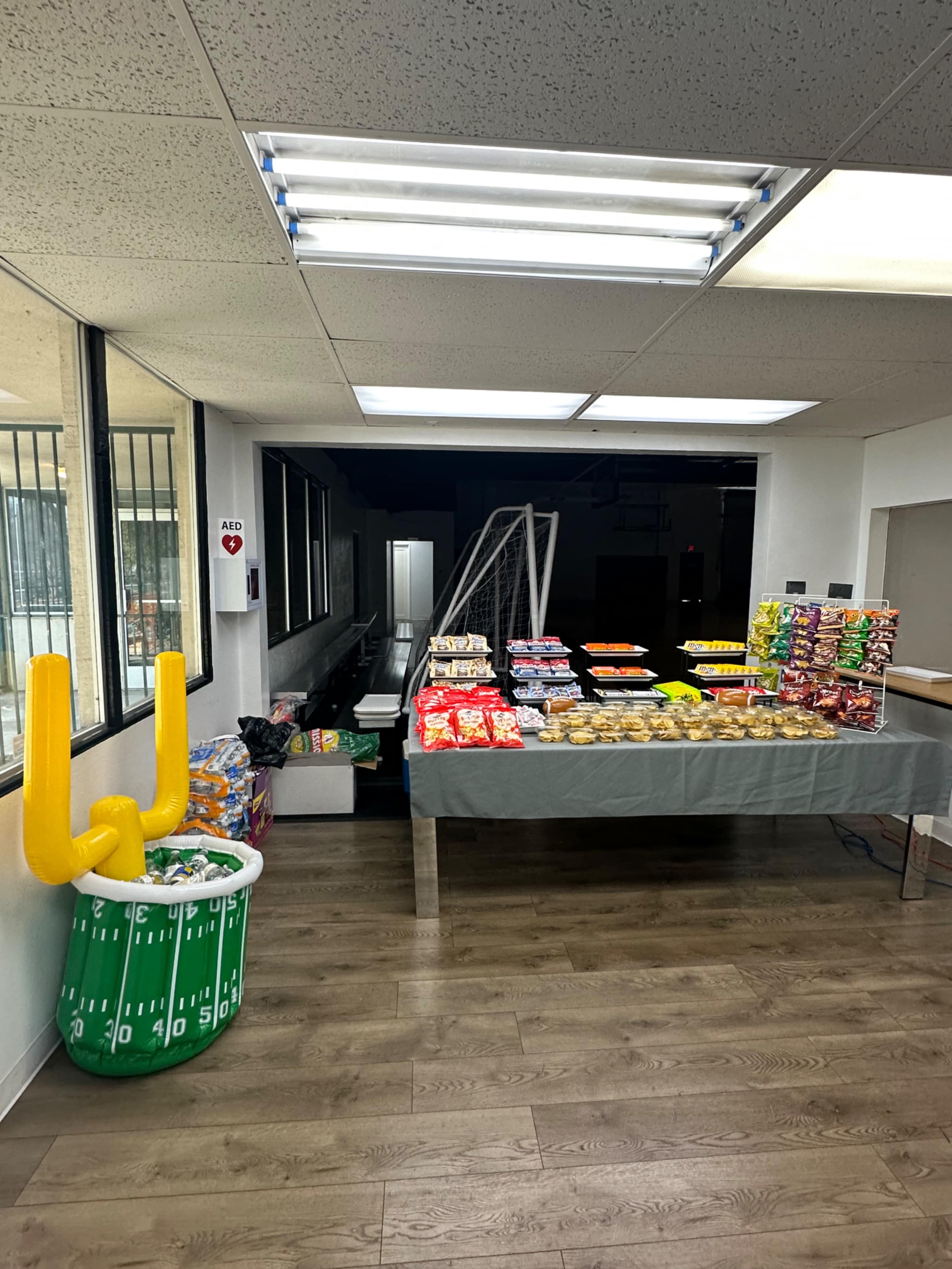 The image shows a room with a table set up with various snacks and treats, alongside a decorative large football-themed item in a green container.