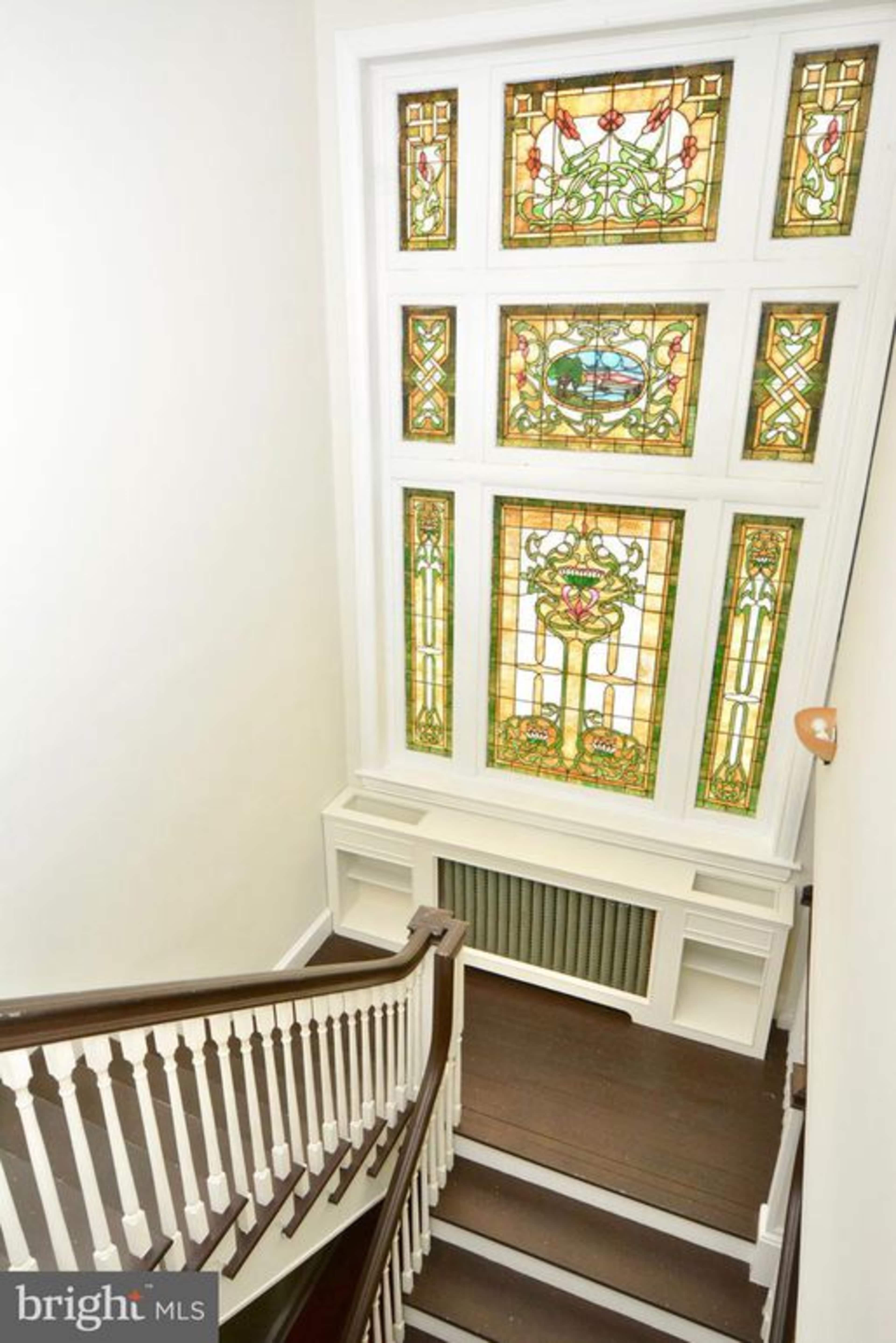 A staircase descends alongside a large, colorful stained glass window.
