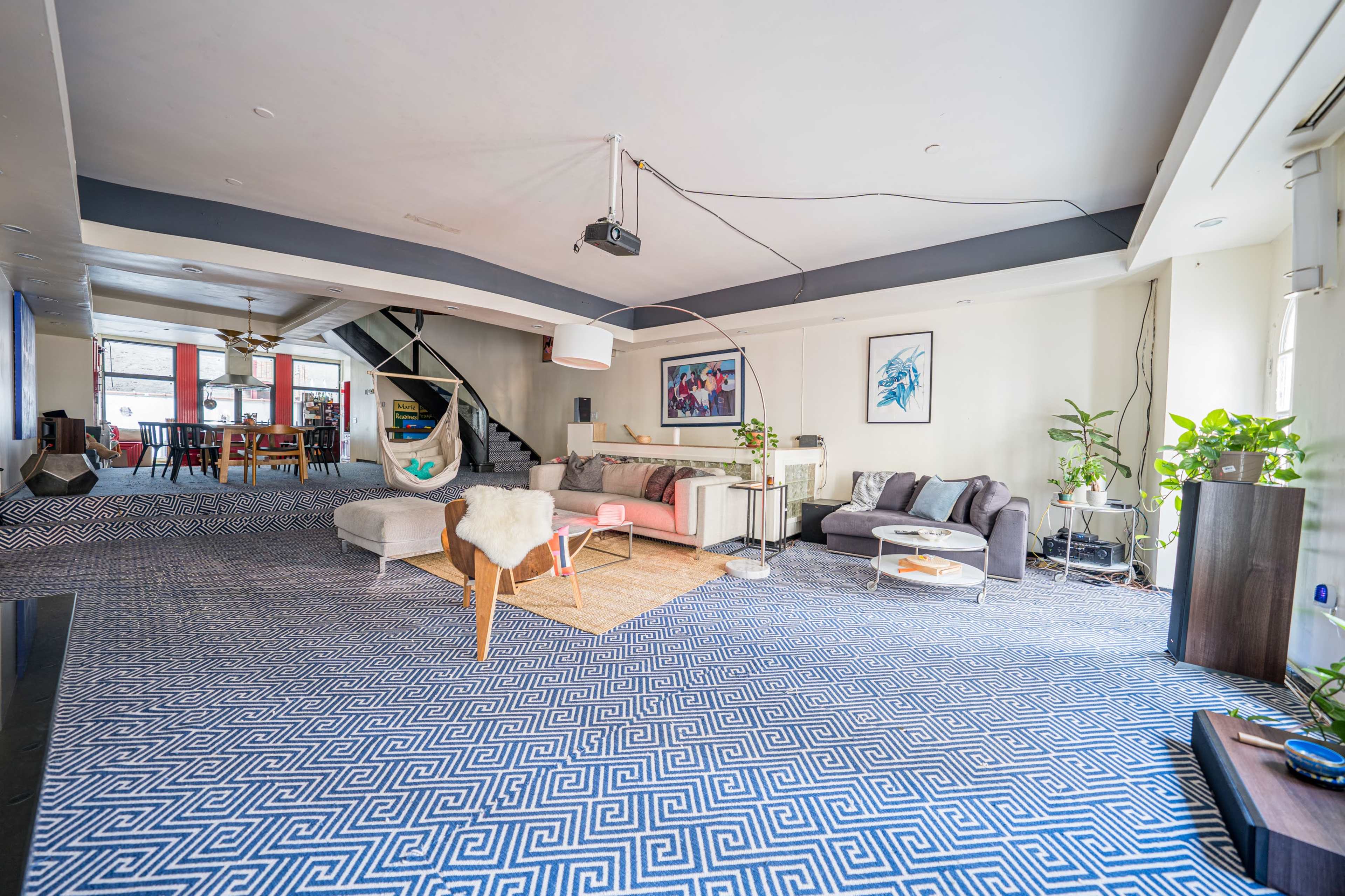 A spacious living area with modern furniture, a large patterned rug, and a staircase in the background.