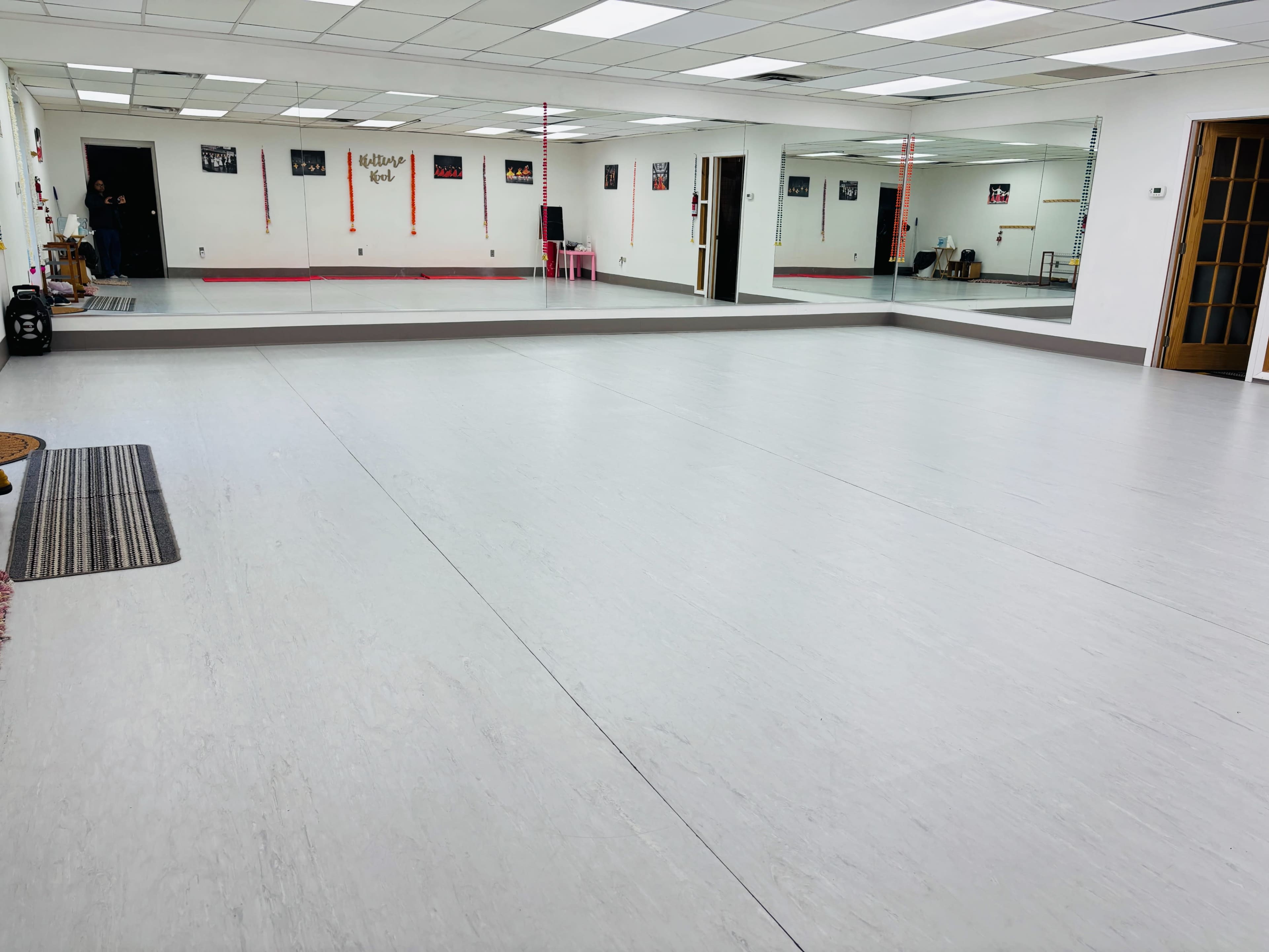 The image shows a spacious, empty dance studio with mirrored walls and wooden flooring.