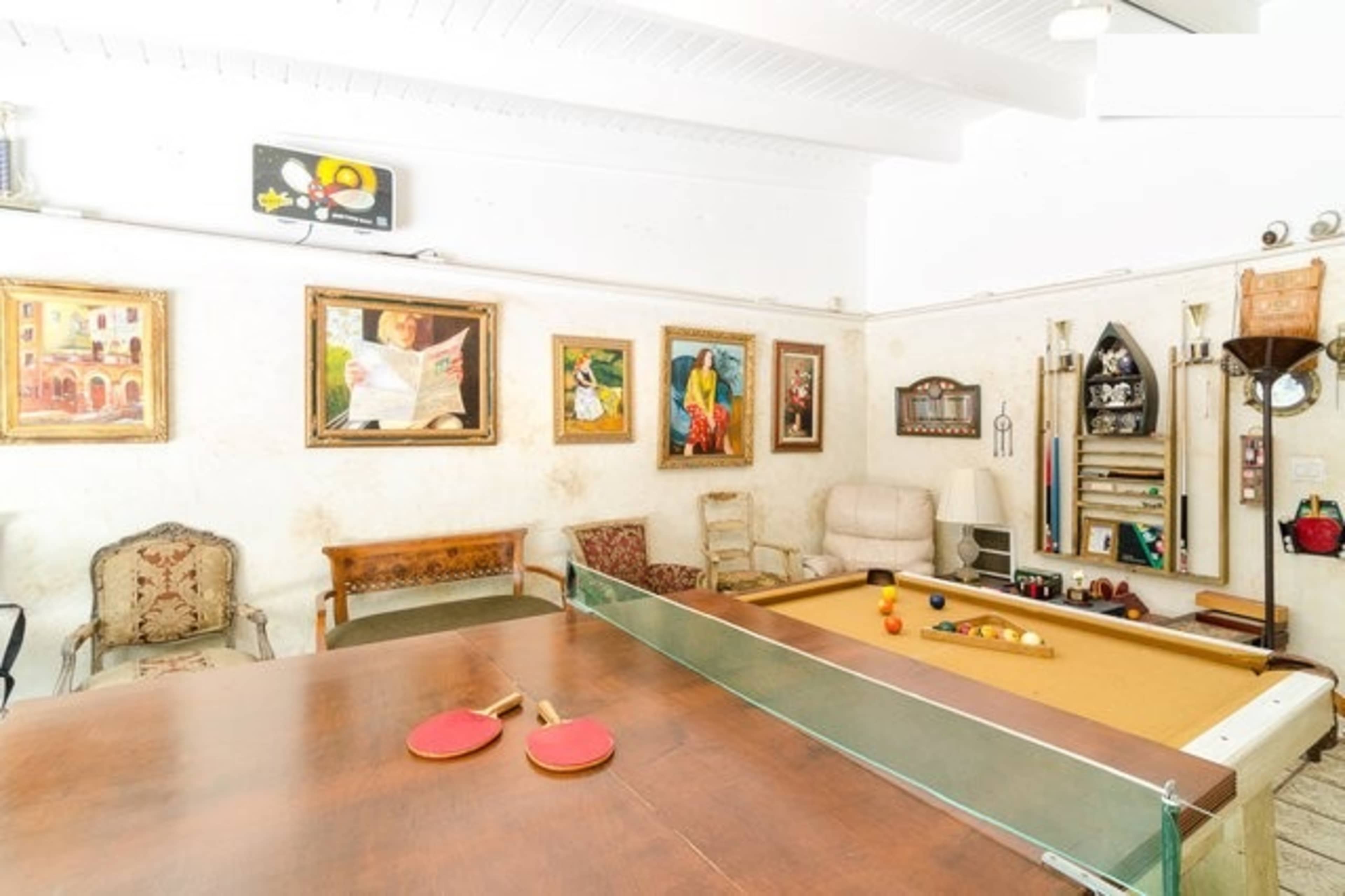 A leisure room with a pool table, ping pong paddles on a wooden table, and several framed artworks on the walls.