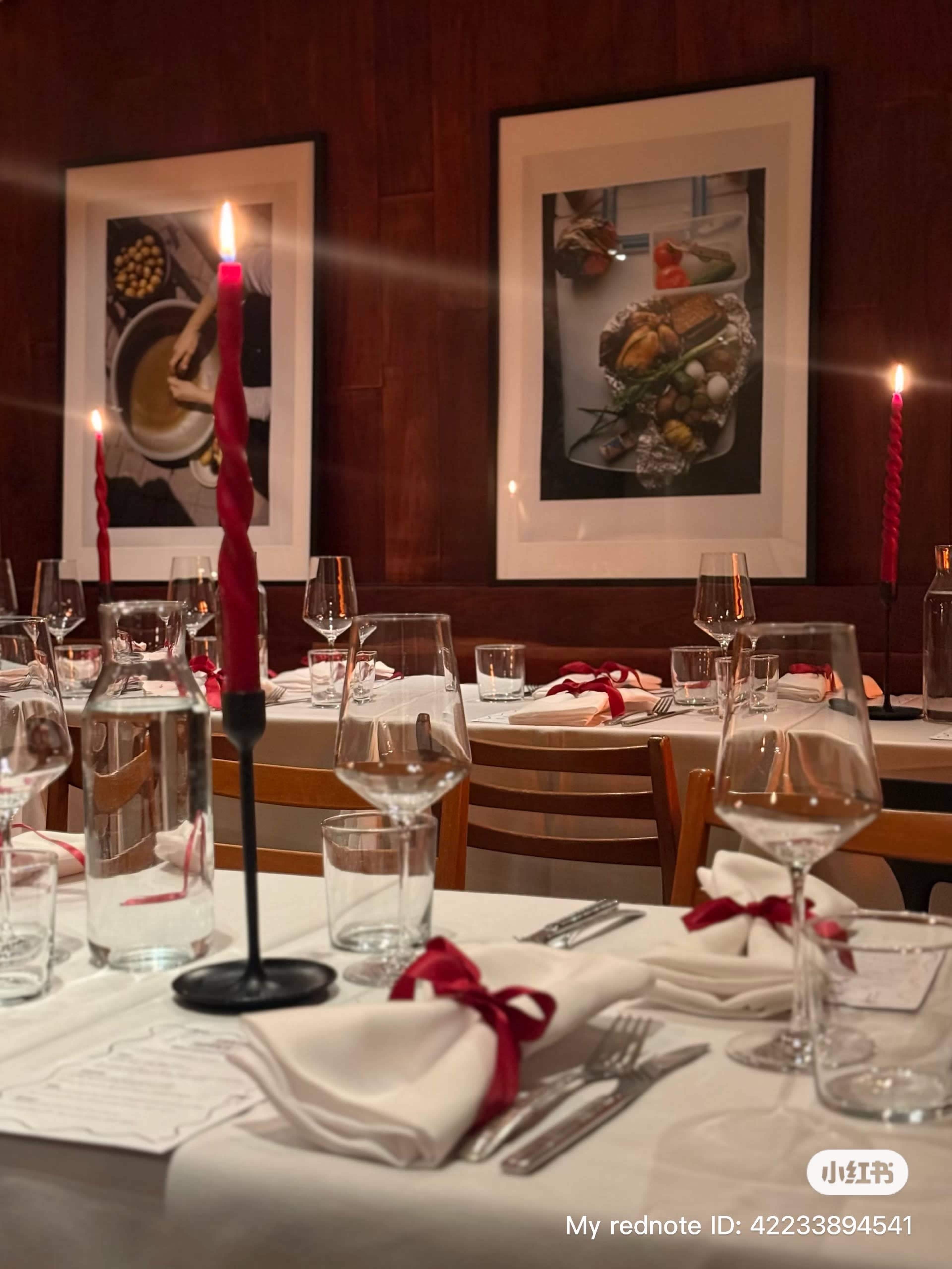 A dining table is set with glasses and red napkins, surrounded by lit candles and framed artwork on the walls.