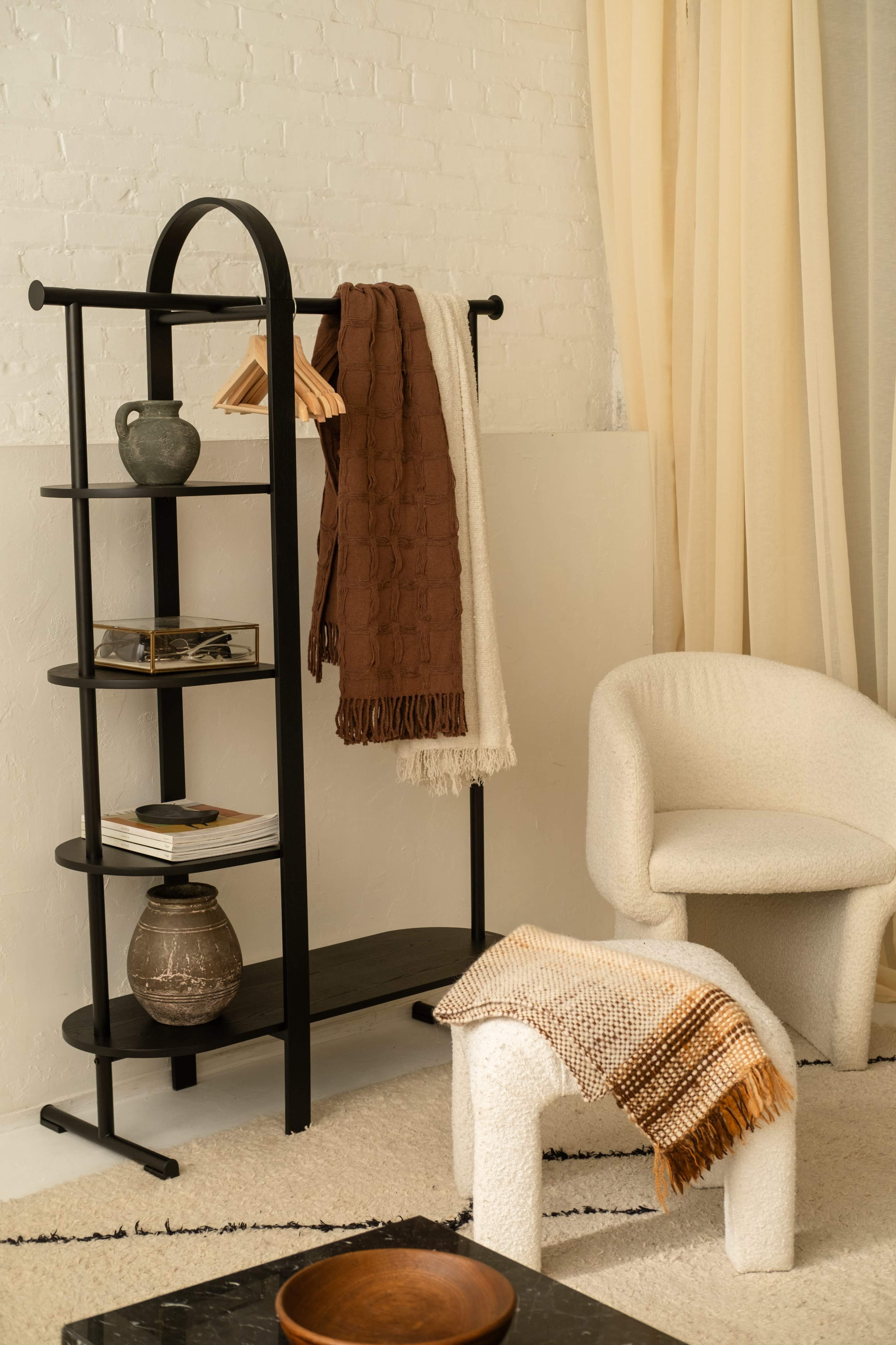 The image features a modern shelf displaying decorative items, with a chair and a textured stool on a light-colored rug.