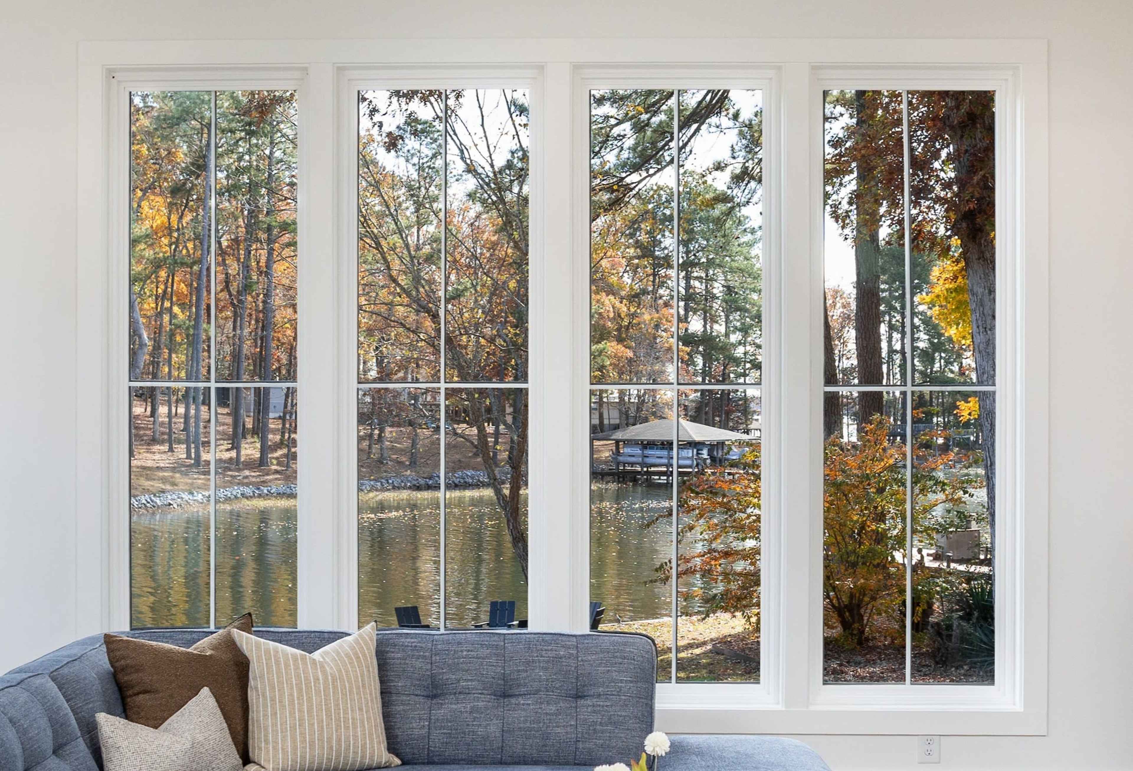 A living room features large windows overlooking a lake surrounded by trees with fall foliage.