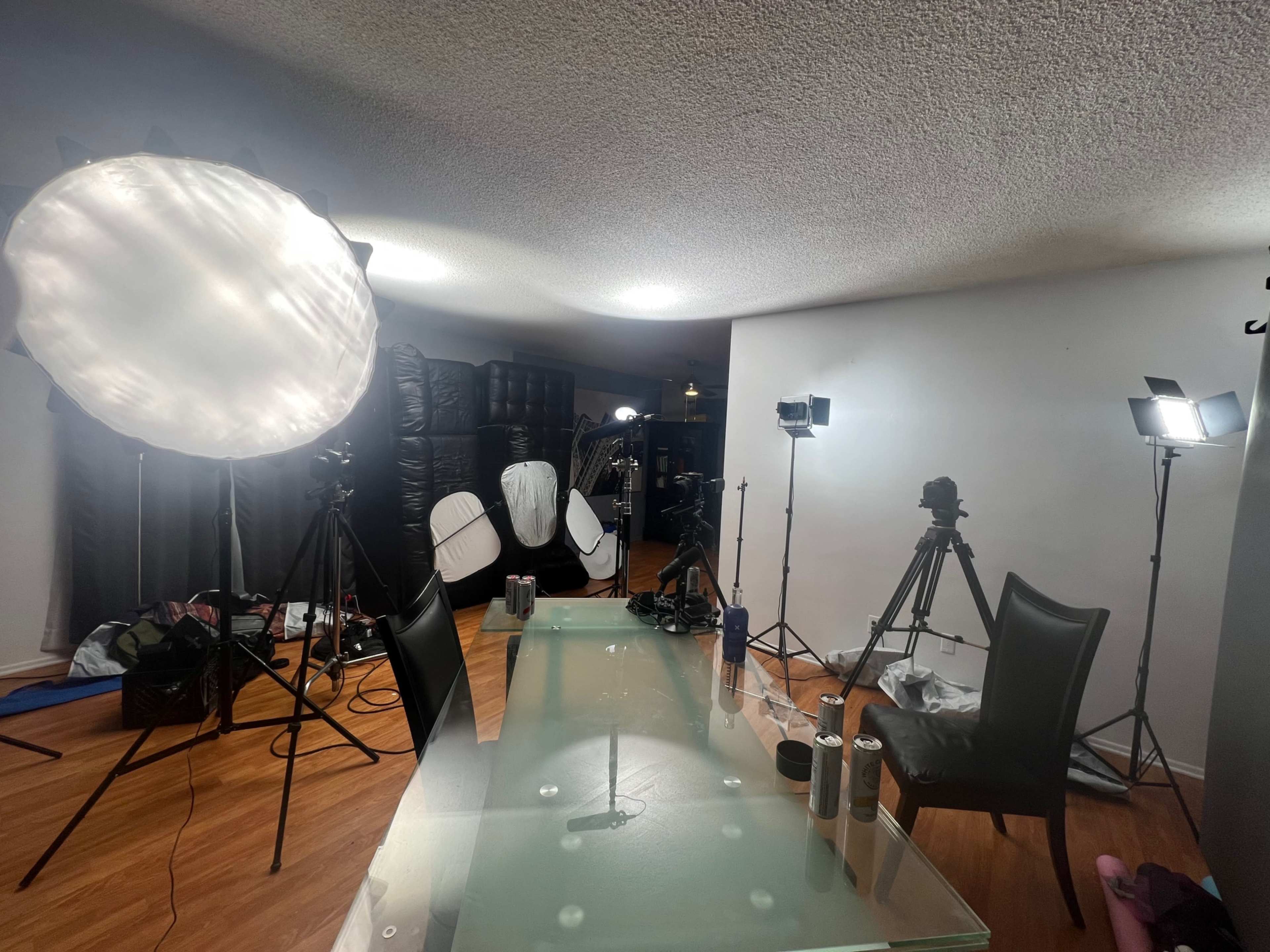 A well-equipped photography studio features multiple lights, camera tripods, and a glass table positioned in the center of the room.