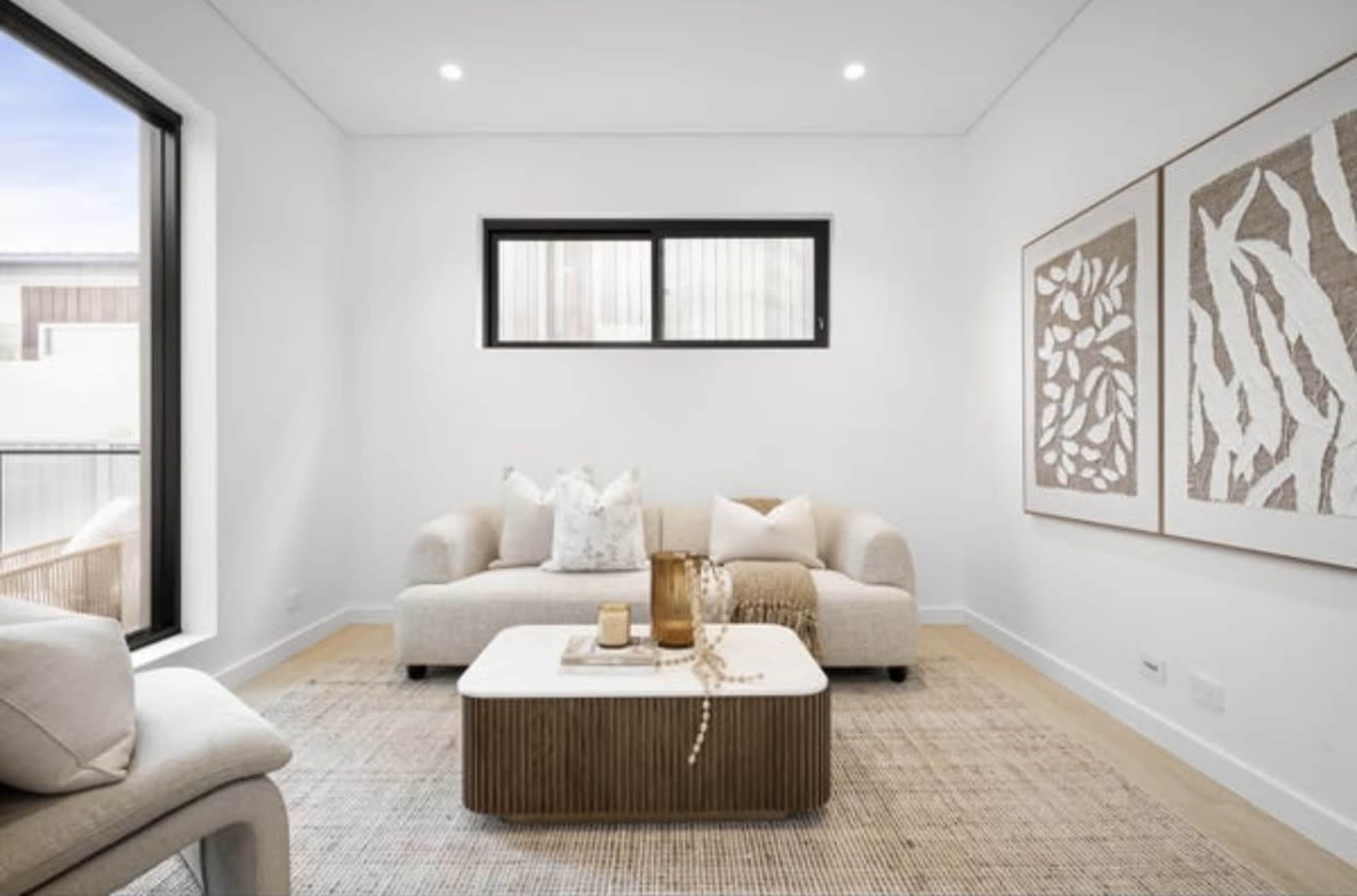 The image shows a minimalistic living room featuring a light-colored sofa, a coffee table, and decorative artwork on the walls.