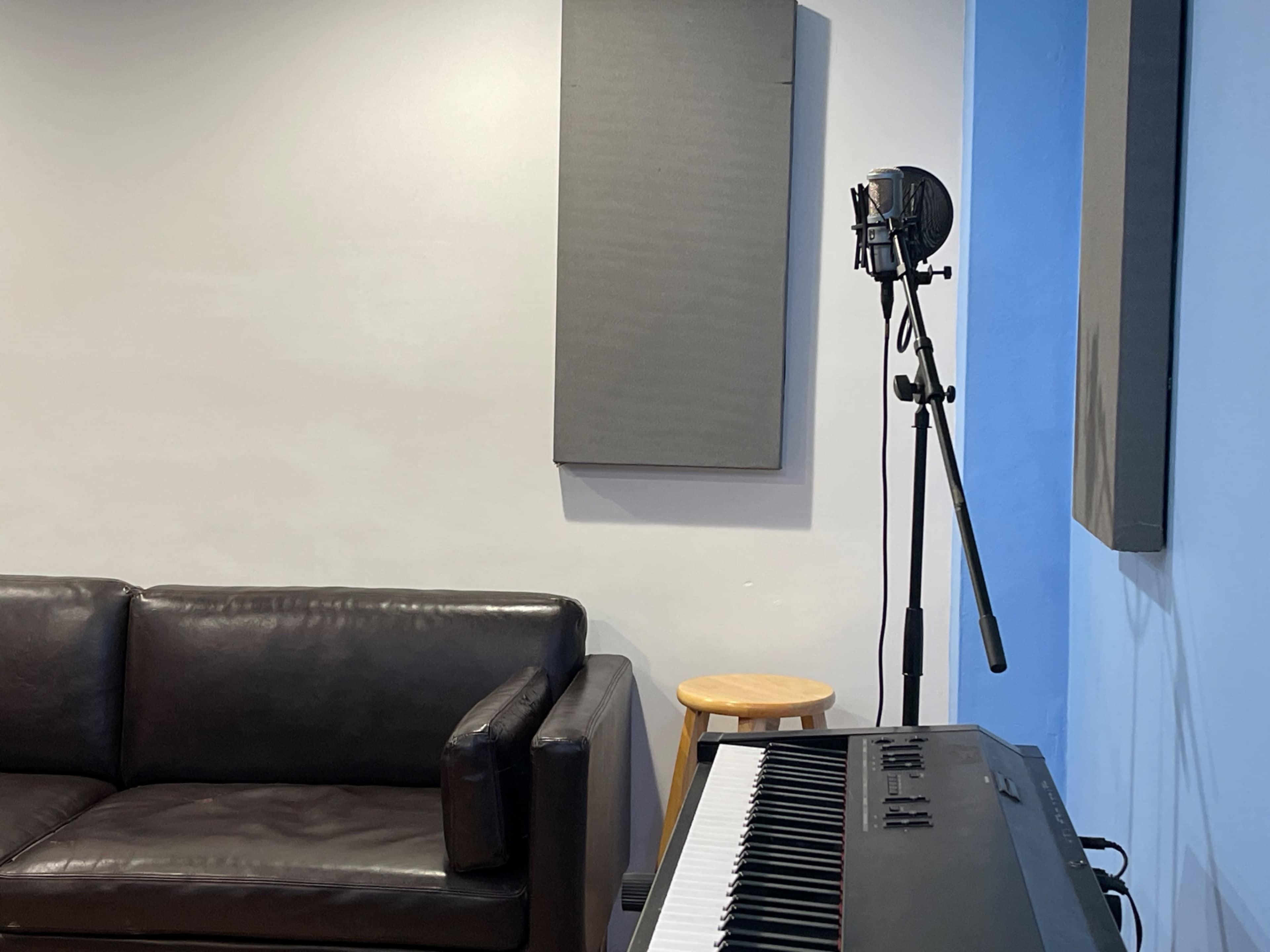A black couch sits beside a keyboard with a microphone on a stand and soundproof panels on the walls.