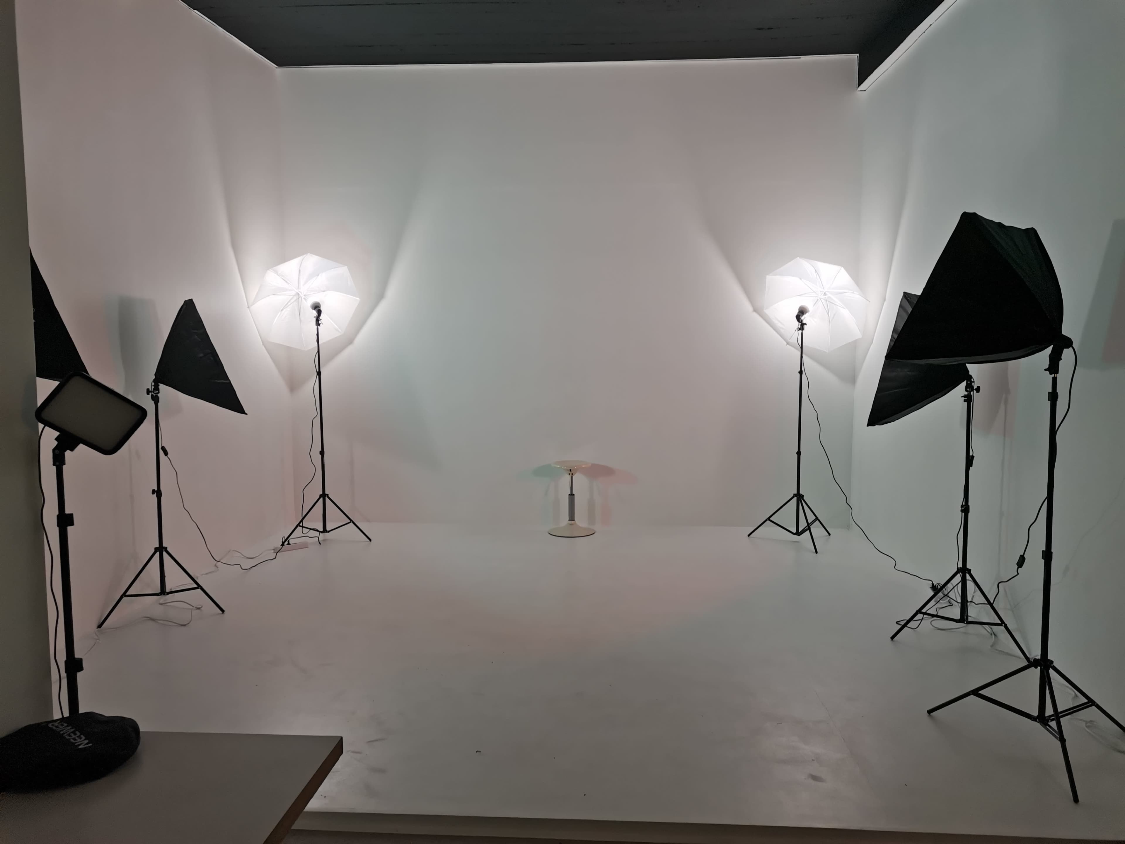 A photography studio features four light stands with umbrellas and a small table in the center on a white floor.