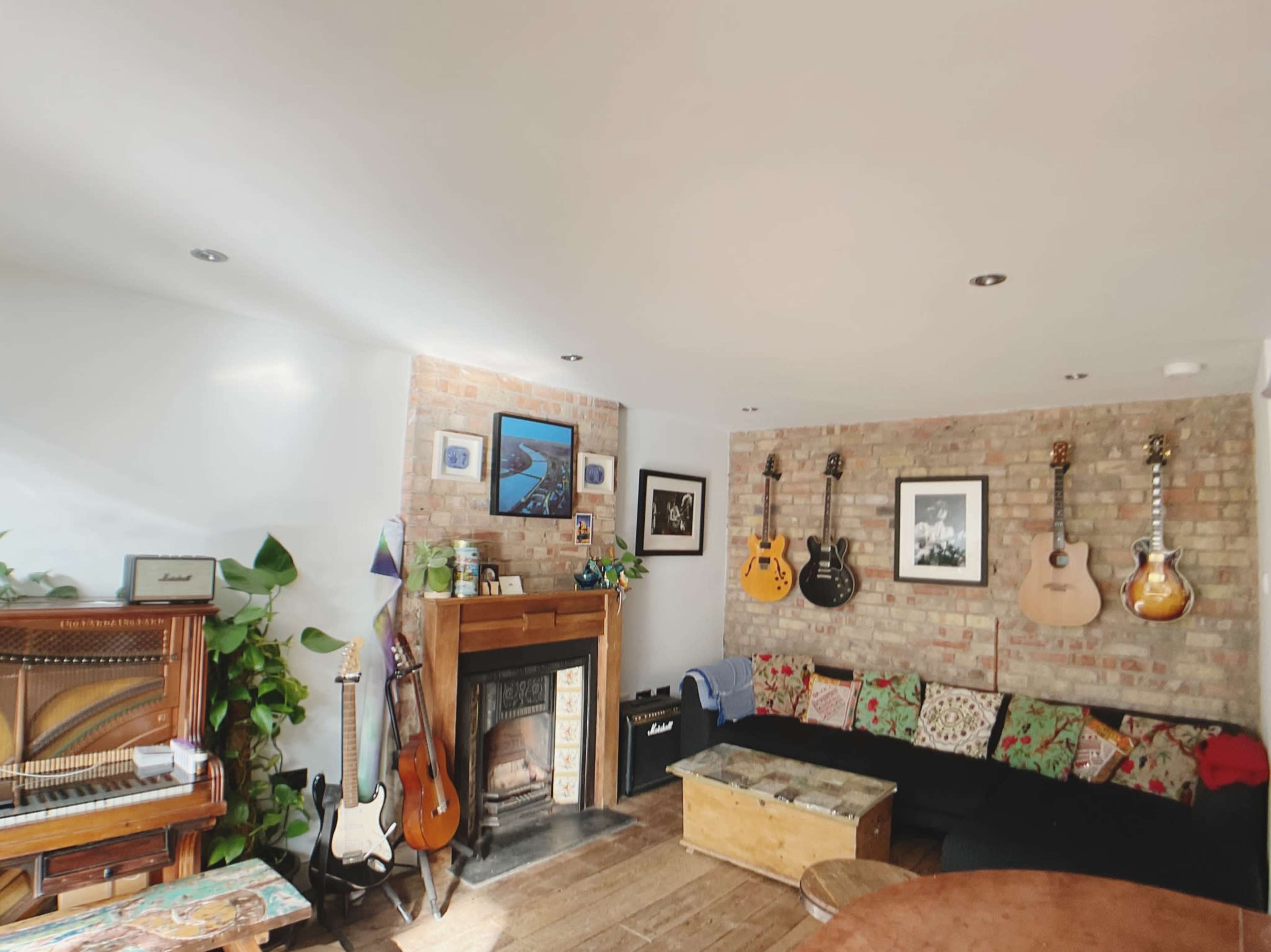 The room features a mix of musical instruments, including guitars and a piano, against a backdrop of exposed brick walls and a decorative fireplace.