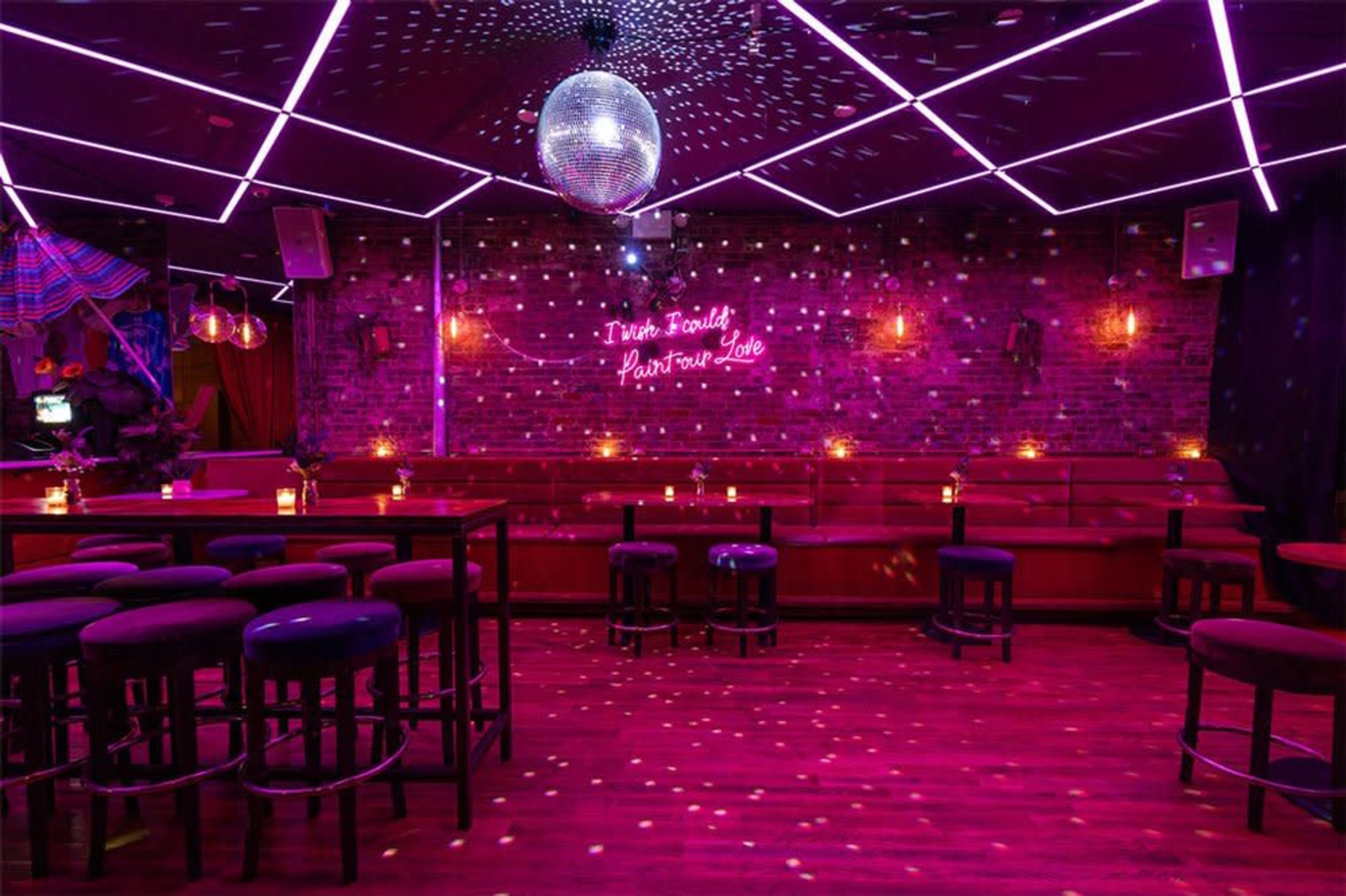 The image shows a dimly lit lounge with purple lighting, a disco ball hanging from the ceiling, and seating arranged along a brick wall.