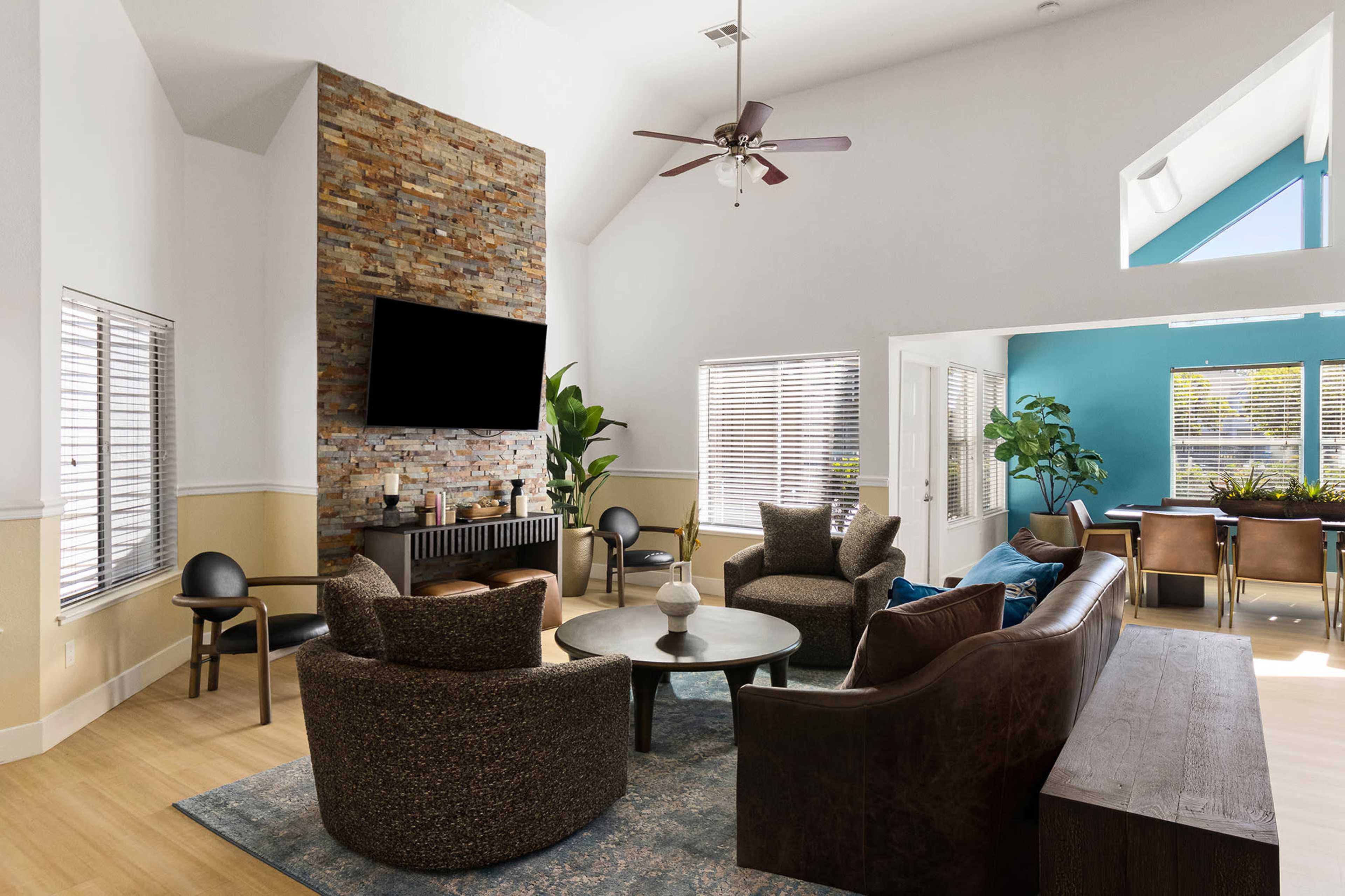 The room features a spacious living area with a stone accent wall, modern furniture, and large windows that provide natural light.