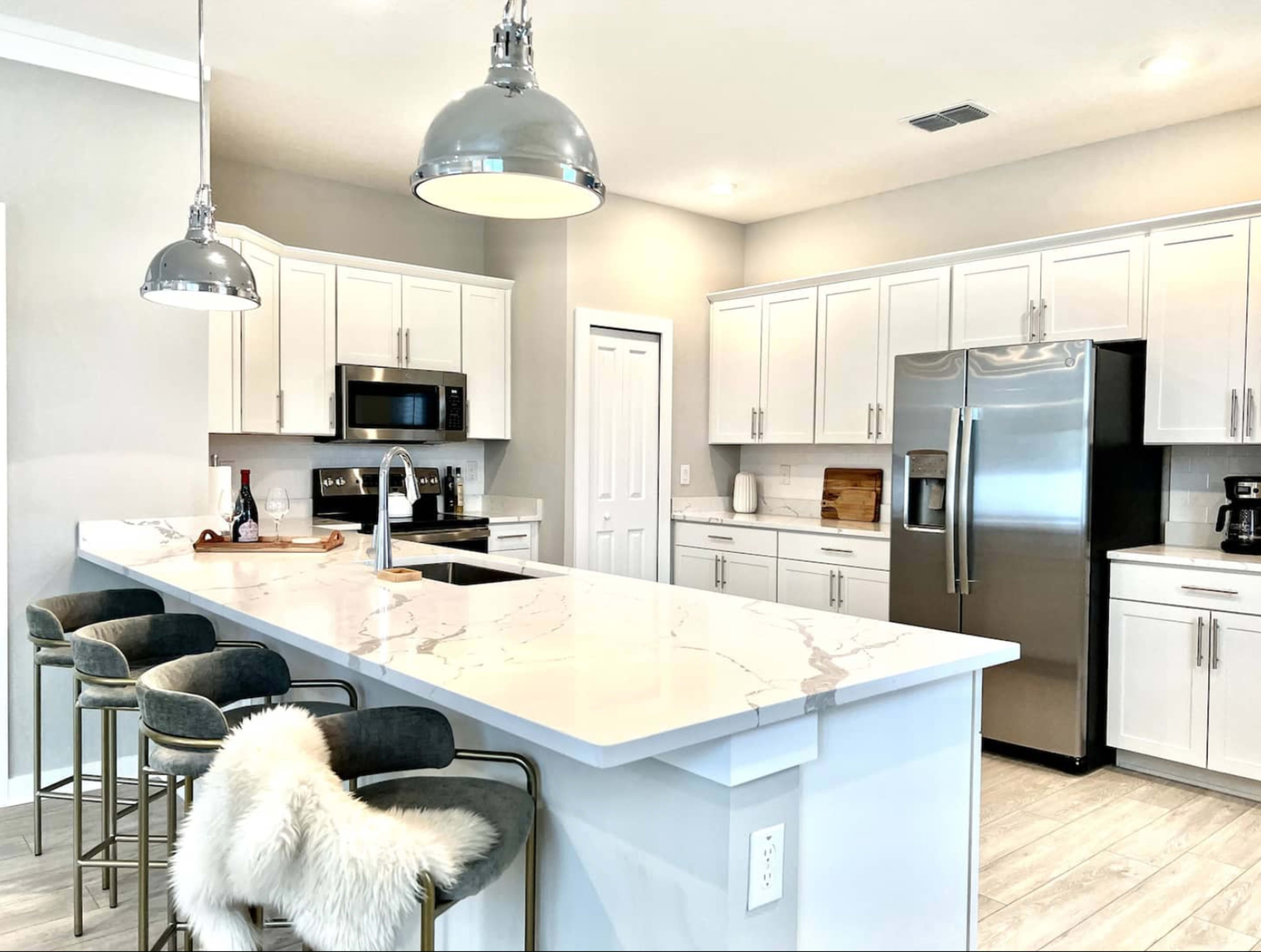 A modern kitchen features white cabinetry, stainless steel appliances, and a large marble-topped island with bar stools.