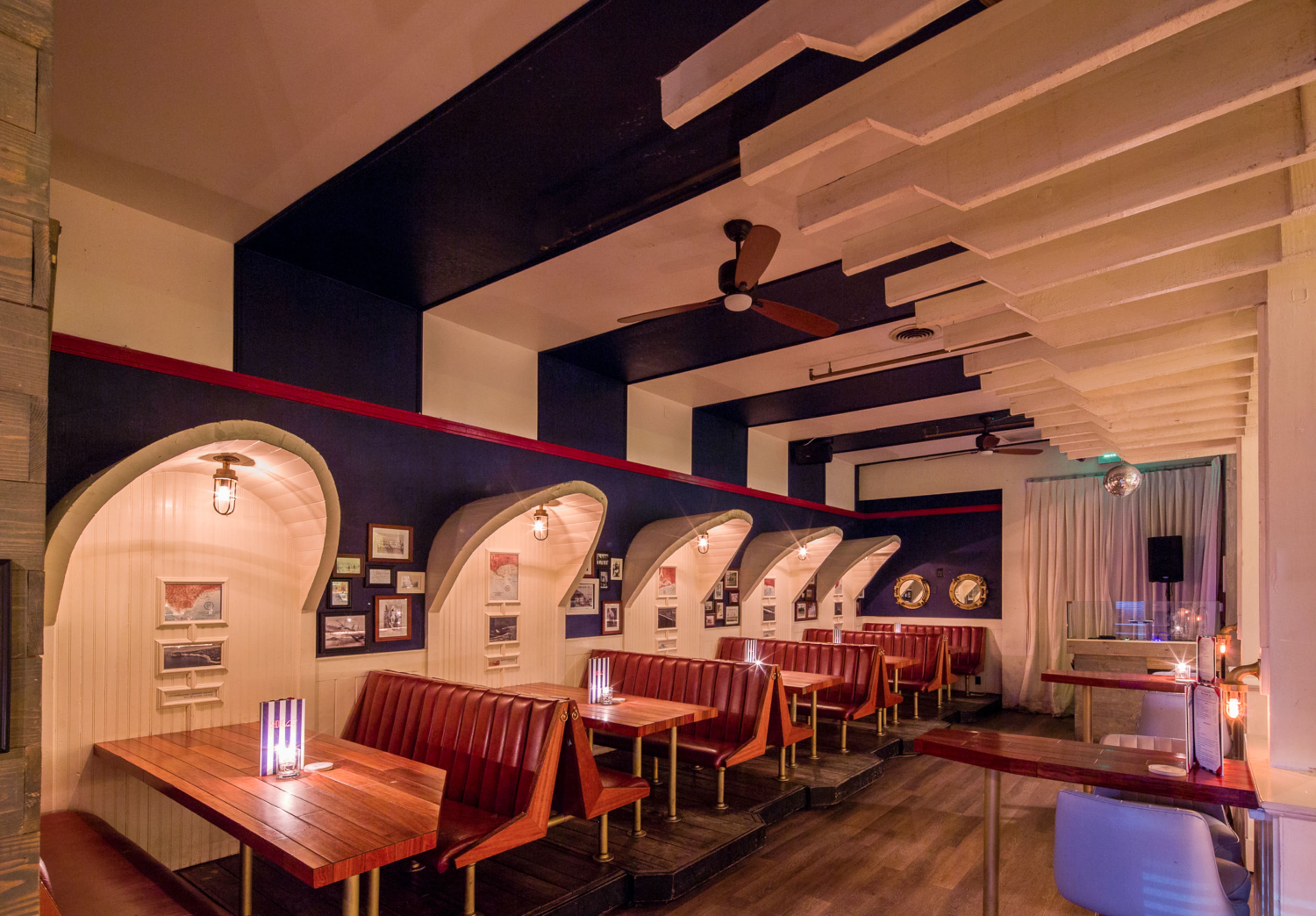 The interior of a restaurant features wooden booths with arched backs, framed pictures on the walls, and ceiling fans.