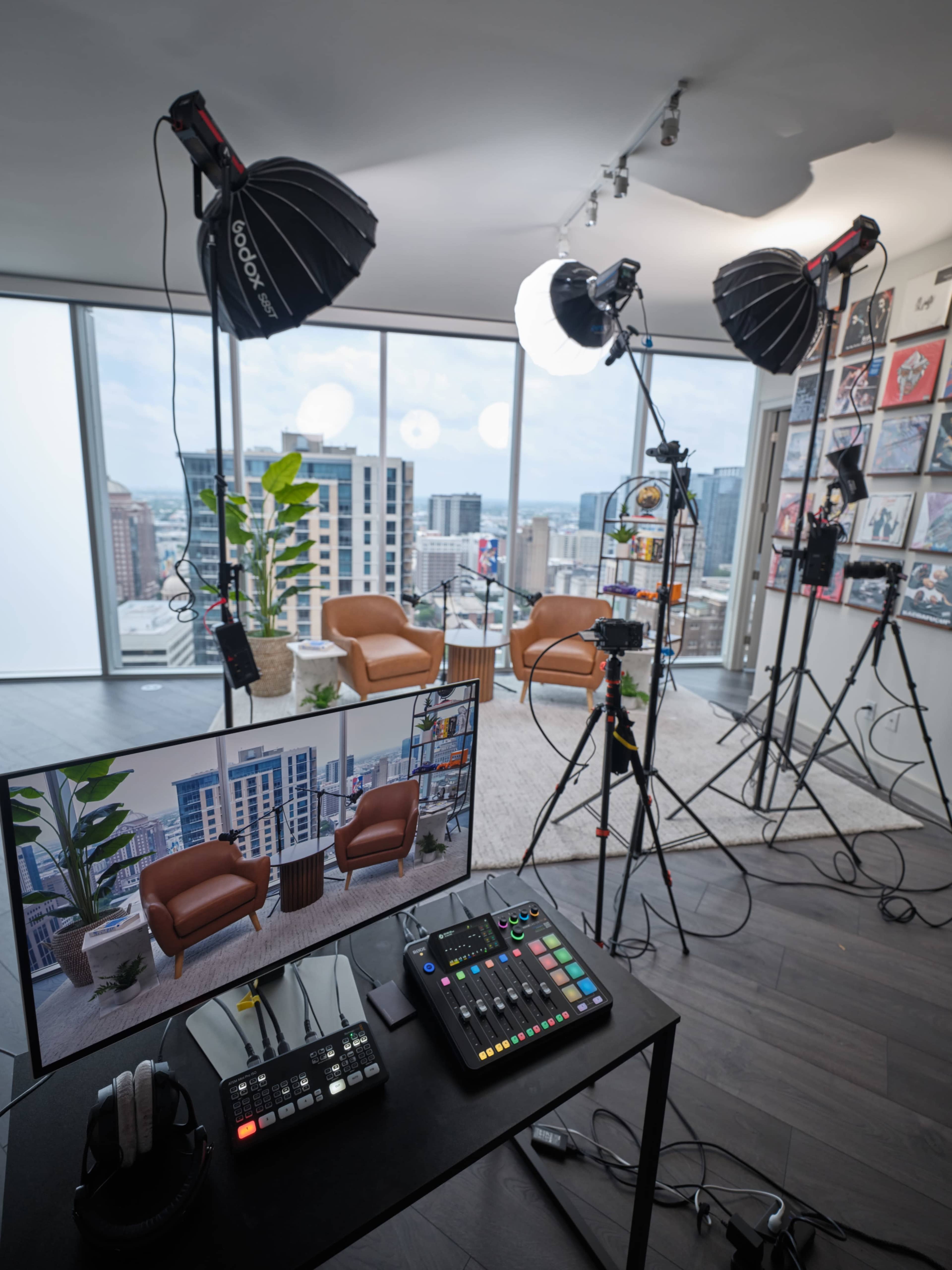 A well-equipped studio setup features two lighting setups, a control panel, and a large screen displaying a virtual background, all within a high-rise apartment.