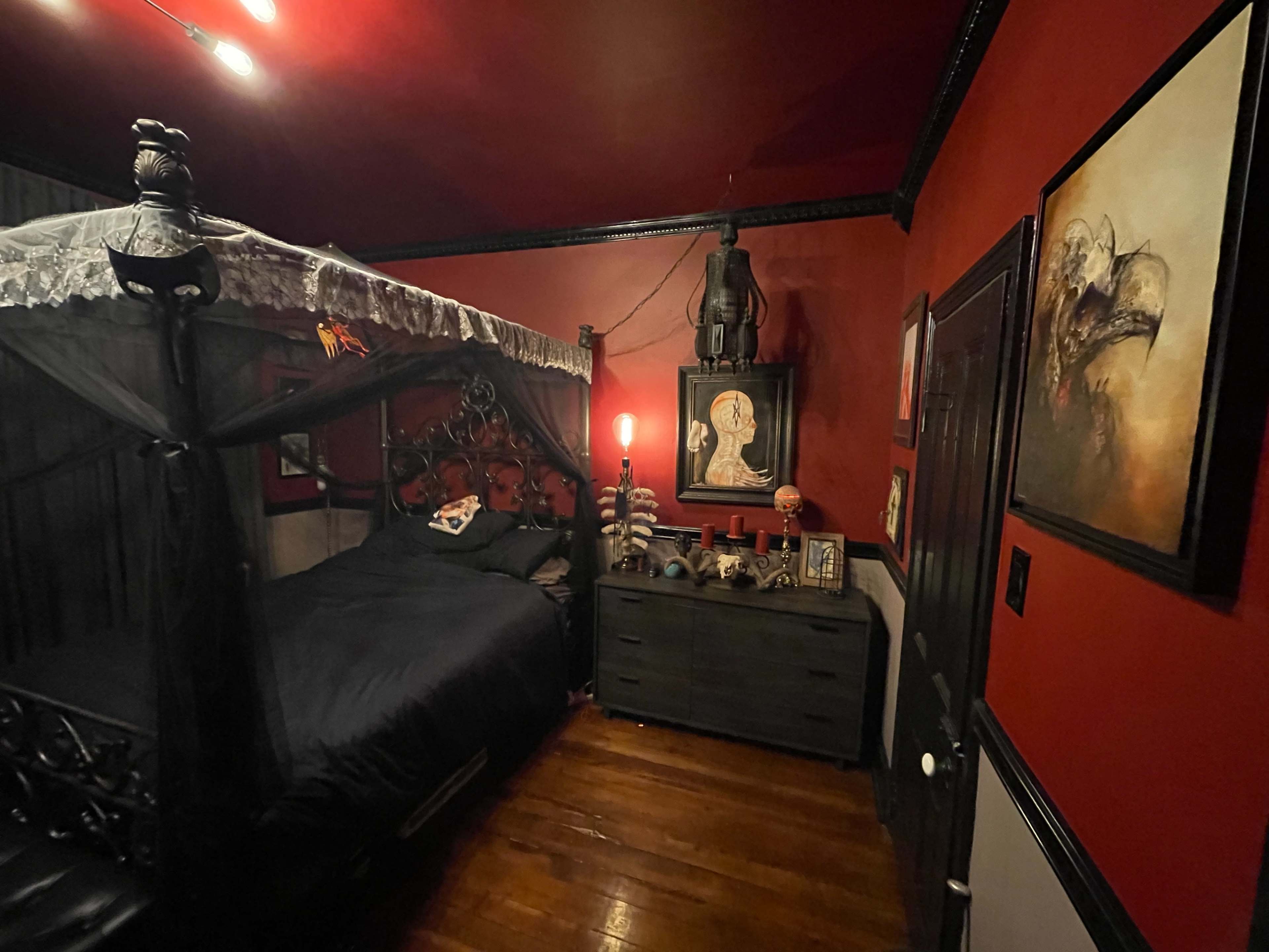 The room features a dark canopy bed against red walls, with a dresser displaying various decorative items.