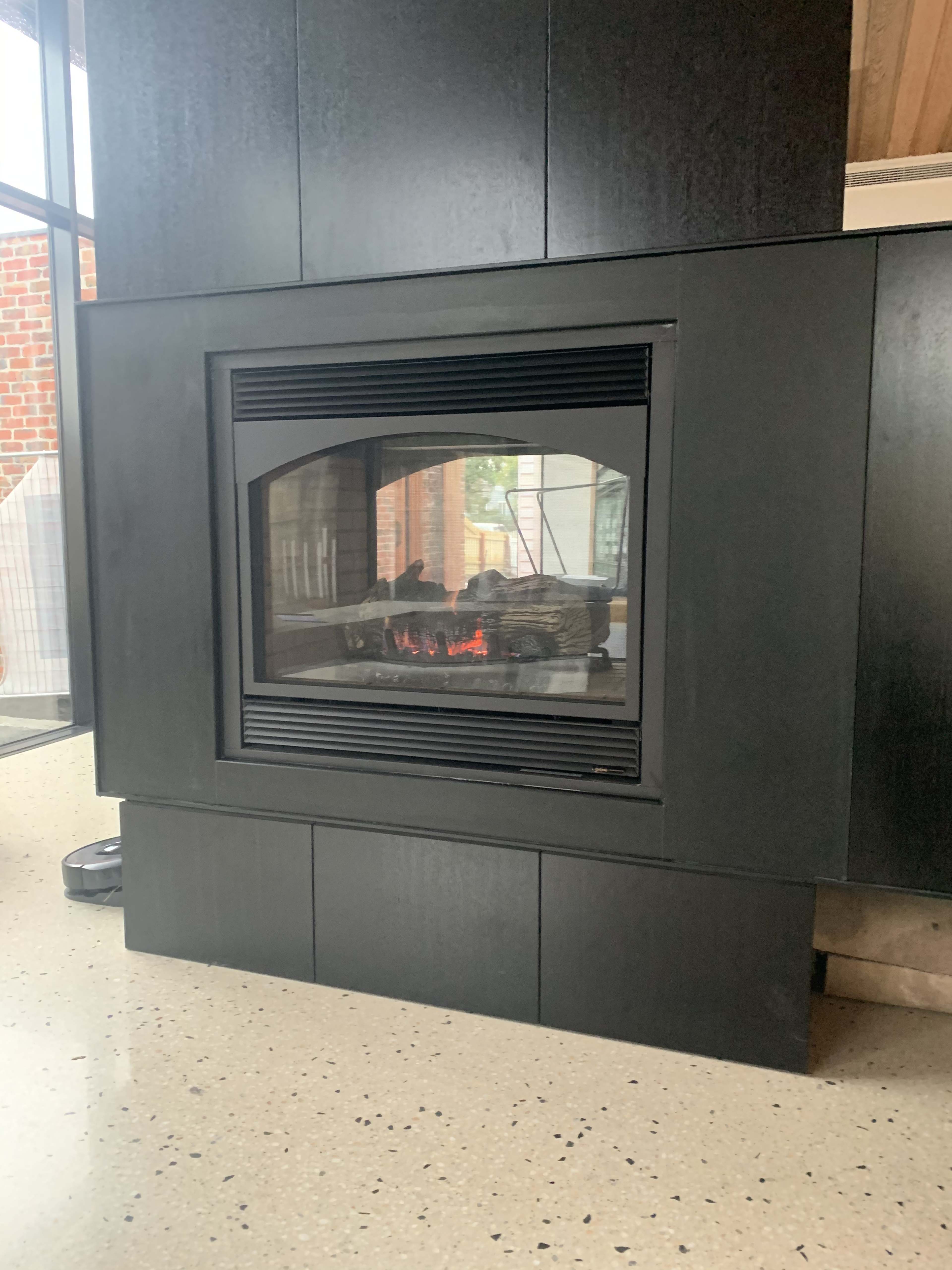 A modern fireplace integrated into a black panel wall with visible logs and glowing embers.